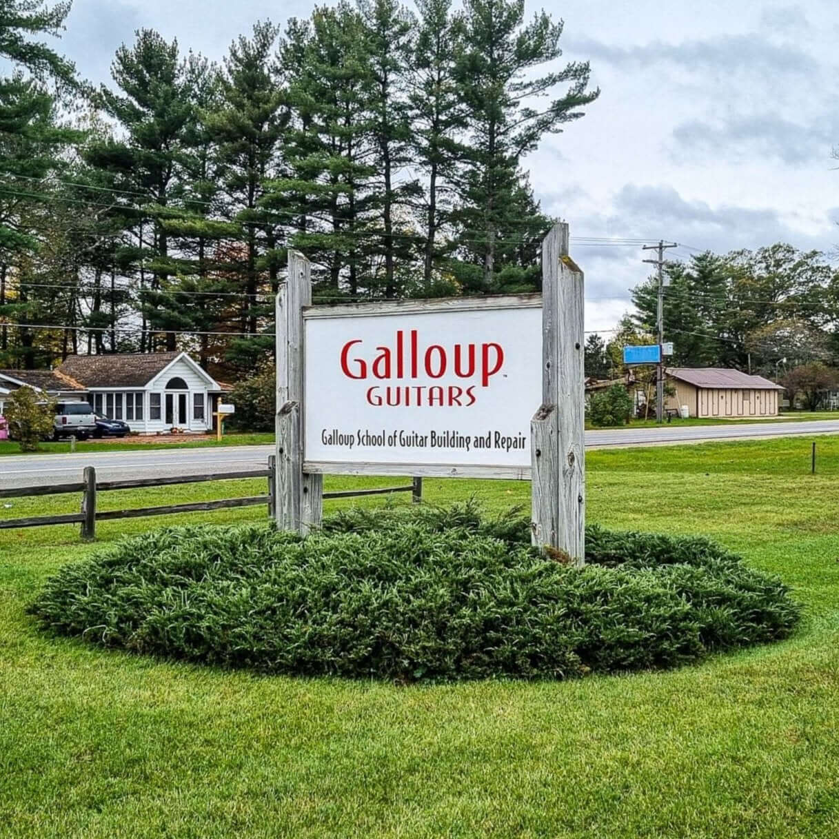Galloup Guitars sign in a grassy area, surrounded by trees, promoting guitar building and repair services.