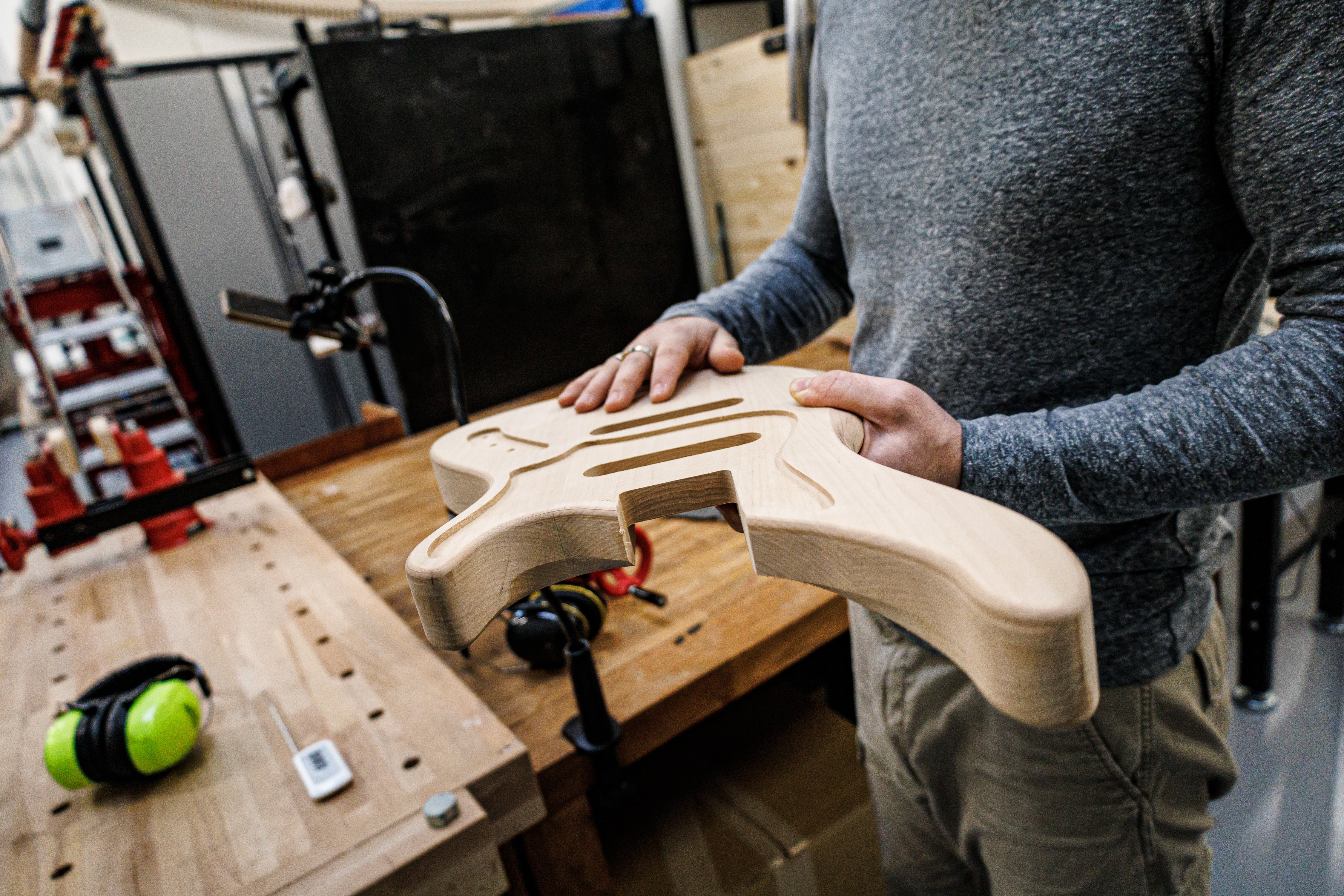 Person working on 6-Week Custom Guitar & Bass Build in Paris, holding a guitar body in a workshop, highlighting lutherie skills.
