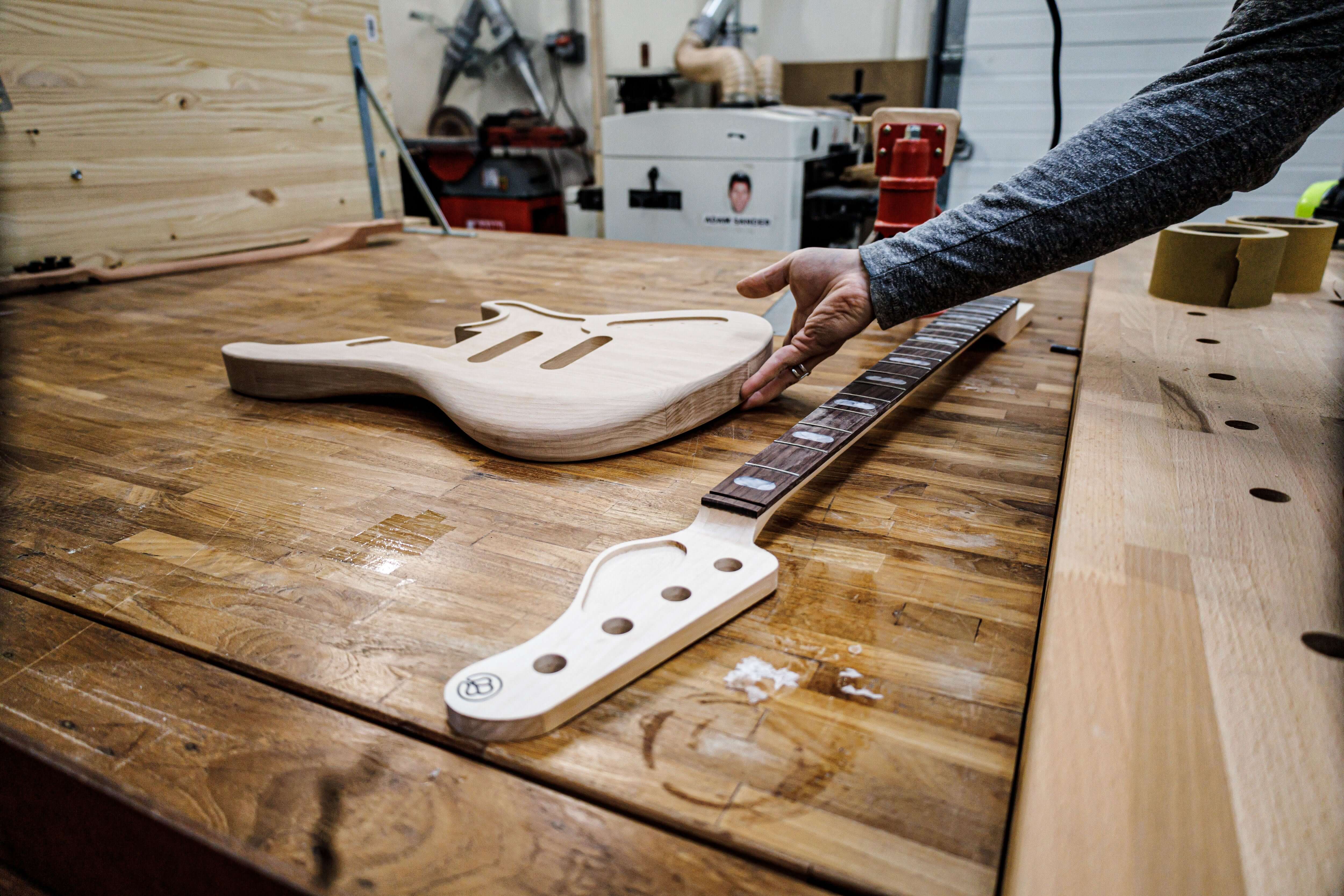 Craftsman assembling Belforti guitar body and neck on wooden workbench in a workshop.