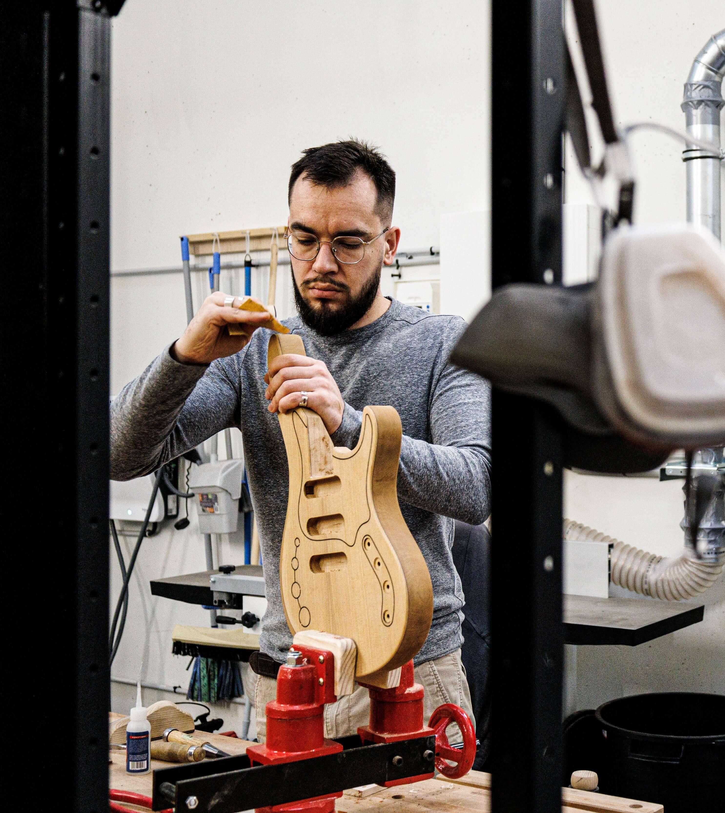 Craftsman shaping guitar body in workshop, focusing on precise detail work, Belforti woodworking.