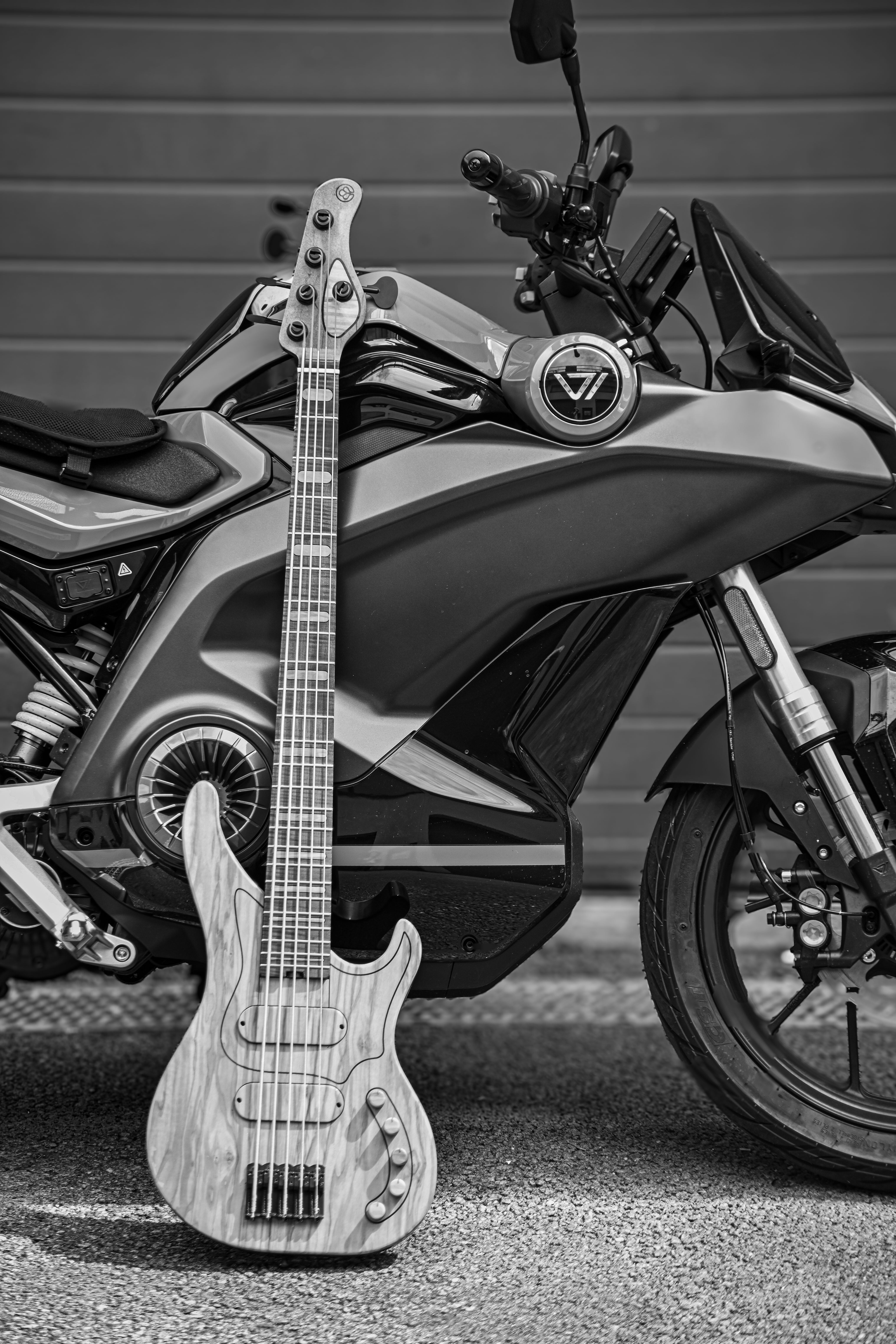 電動VMoto Stashバイクの上に置かれたBelforti M3 Olive 5弦ベースのモノクロ写真。
