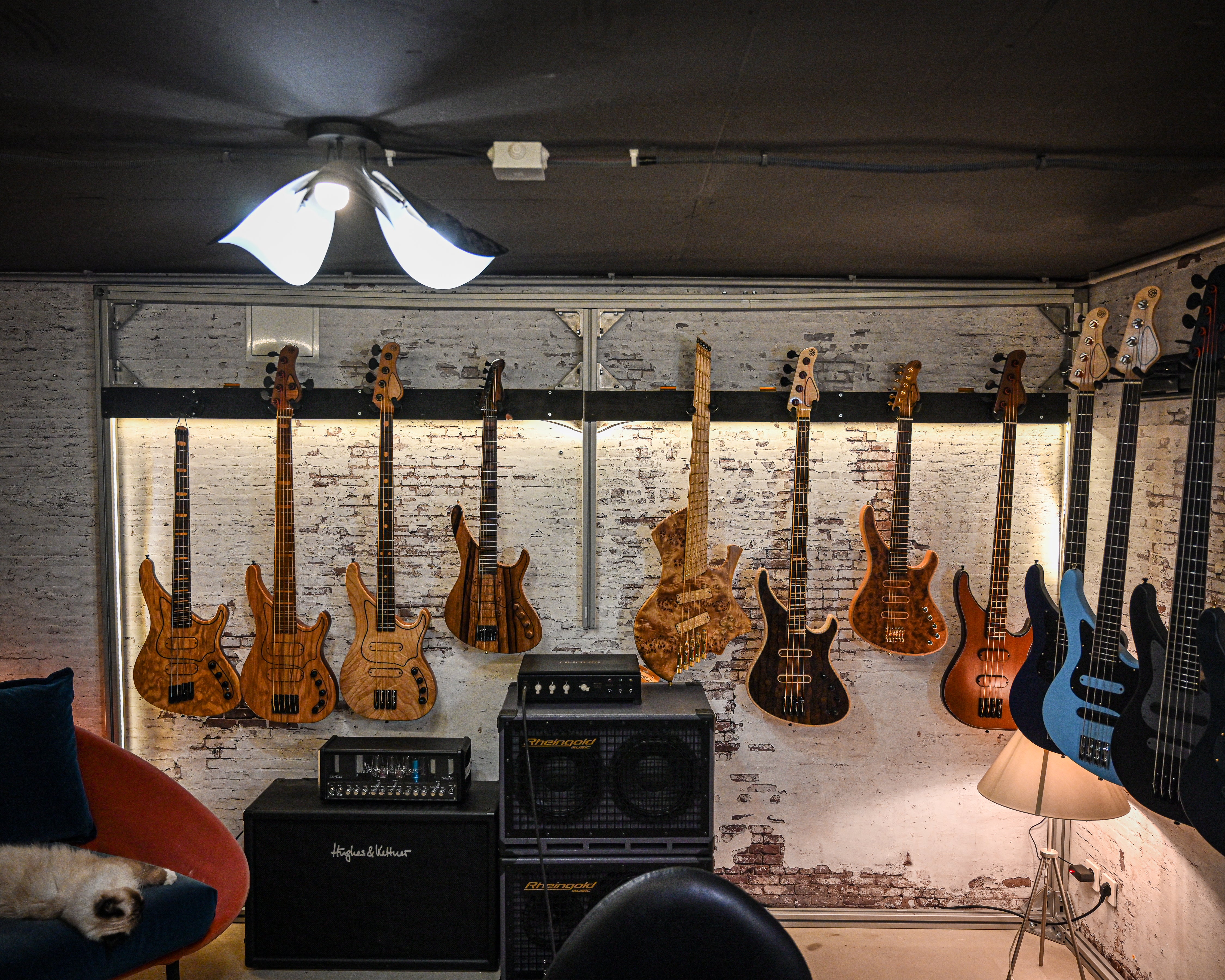 어둑한 음악 스튜디오의 벽돌 벽에 걸려 있는 벨포르티 일렉트릭 기타 컬렉션과, 전경에 놓인 앰프와 아늑한 의자.