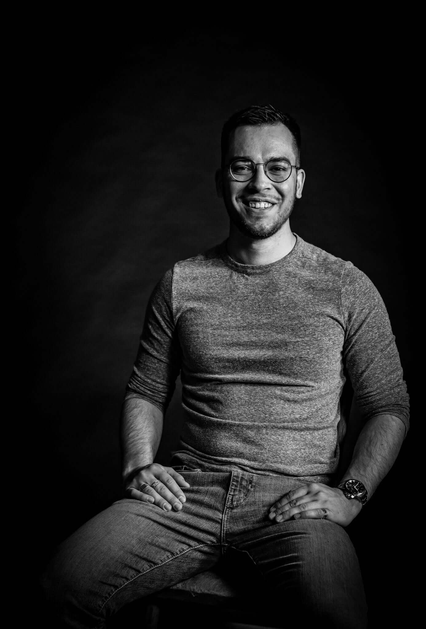 Black and white photo of luthier Marin Nourry-Belforti smiling and sitting, wearing glasses and a casual outfit.