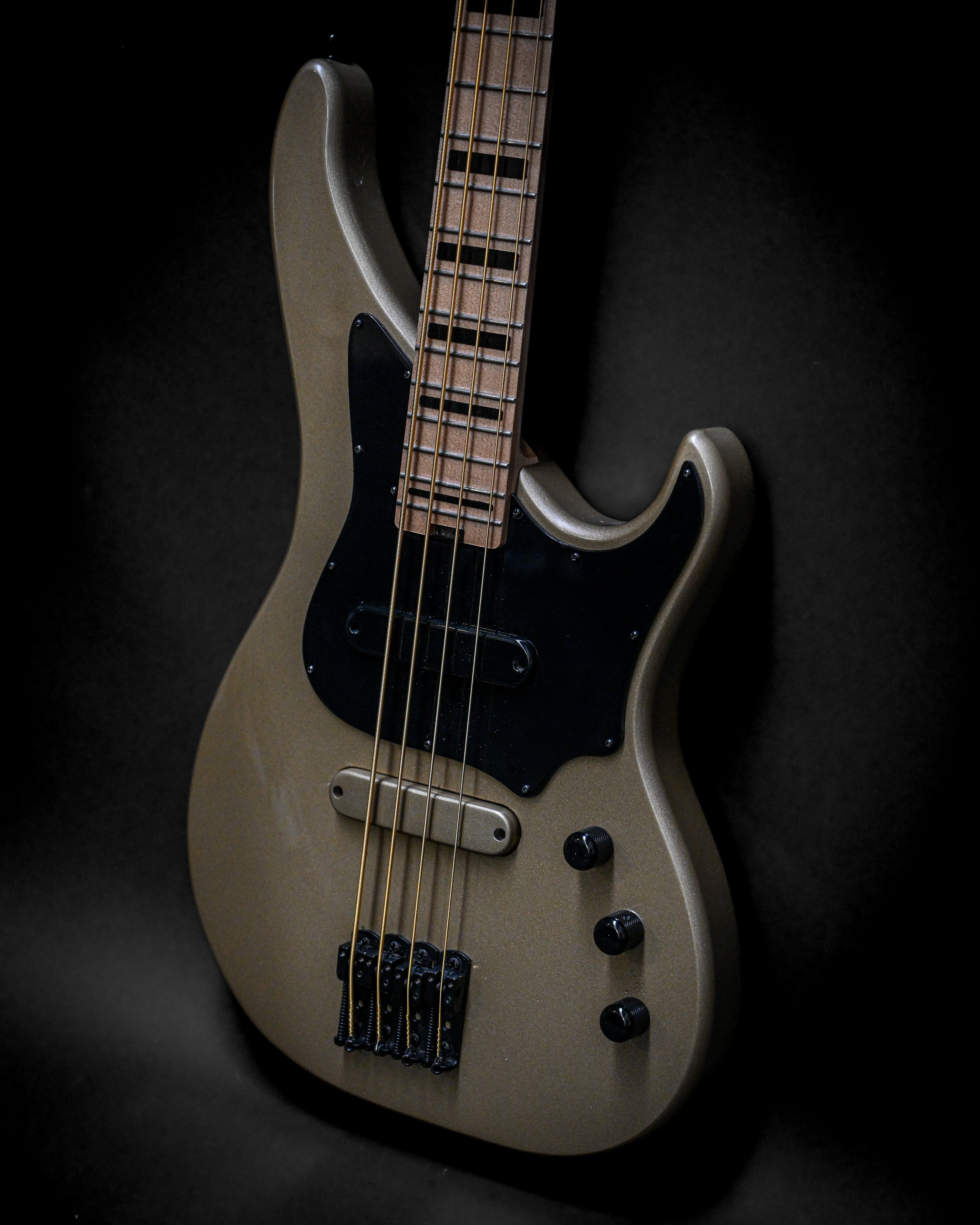 Close-up of a sleek electric bass guitar with four strings, black pickguard, and wooden neck against a dark background.