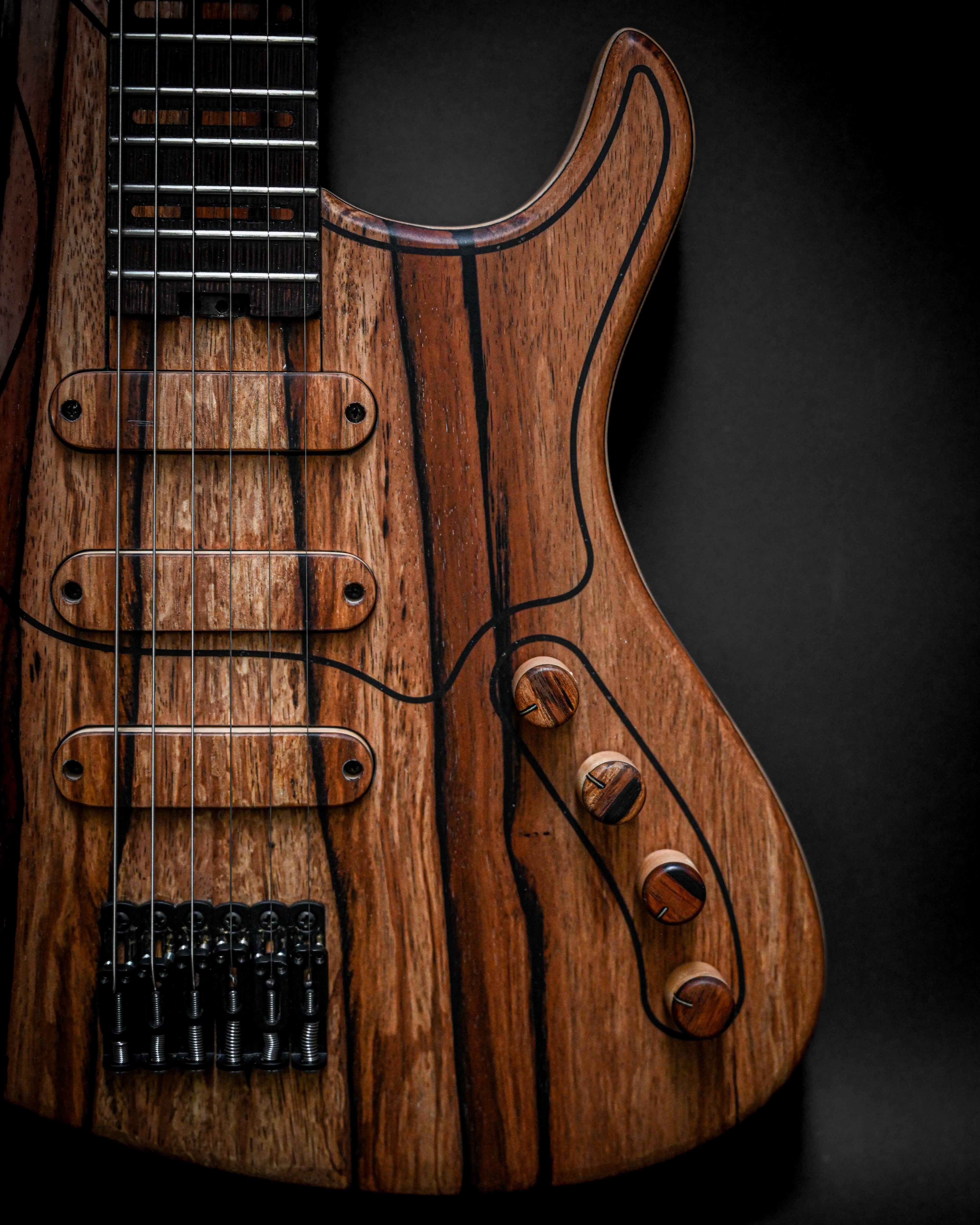 Close-up of a wooden electric guitar body with detailed grain and six strings on a dark background.