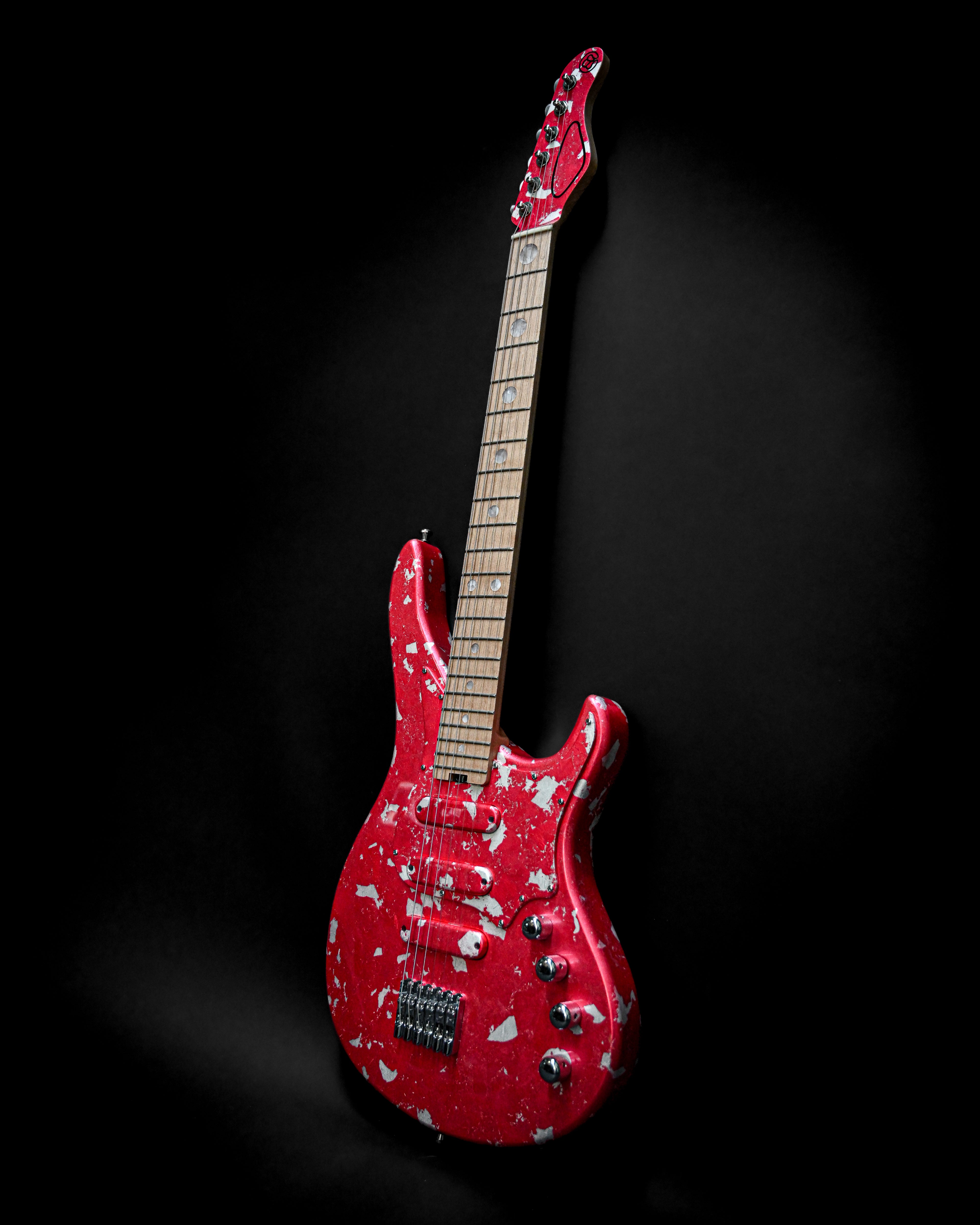 Red electric guitar with a worn finish and black background, highlighting vintage style and unique design.