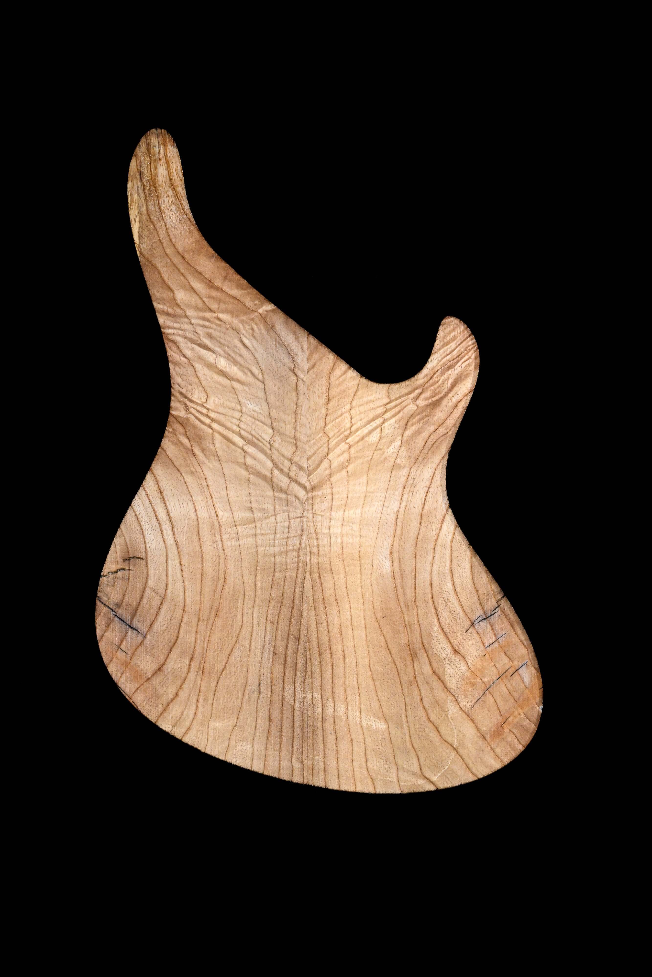 Wooden guitar body shape on black background, showcasing natural grain texture.