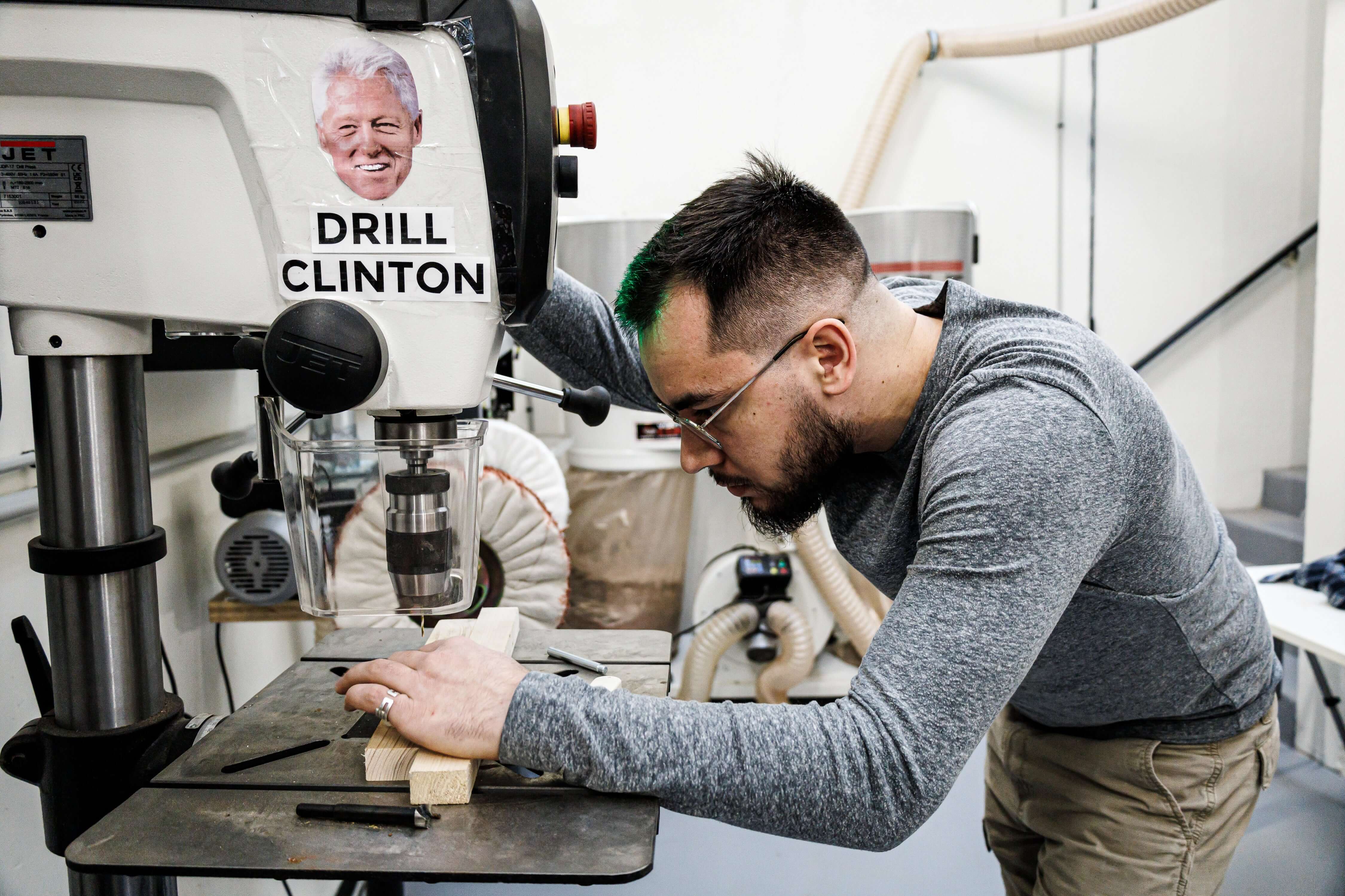 Man using a drill in a workshop with a humorous sticker, focused on precision work.