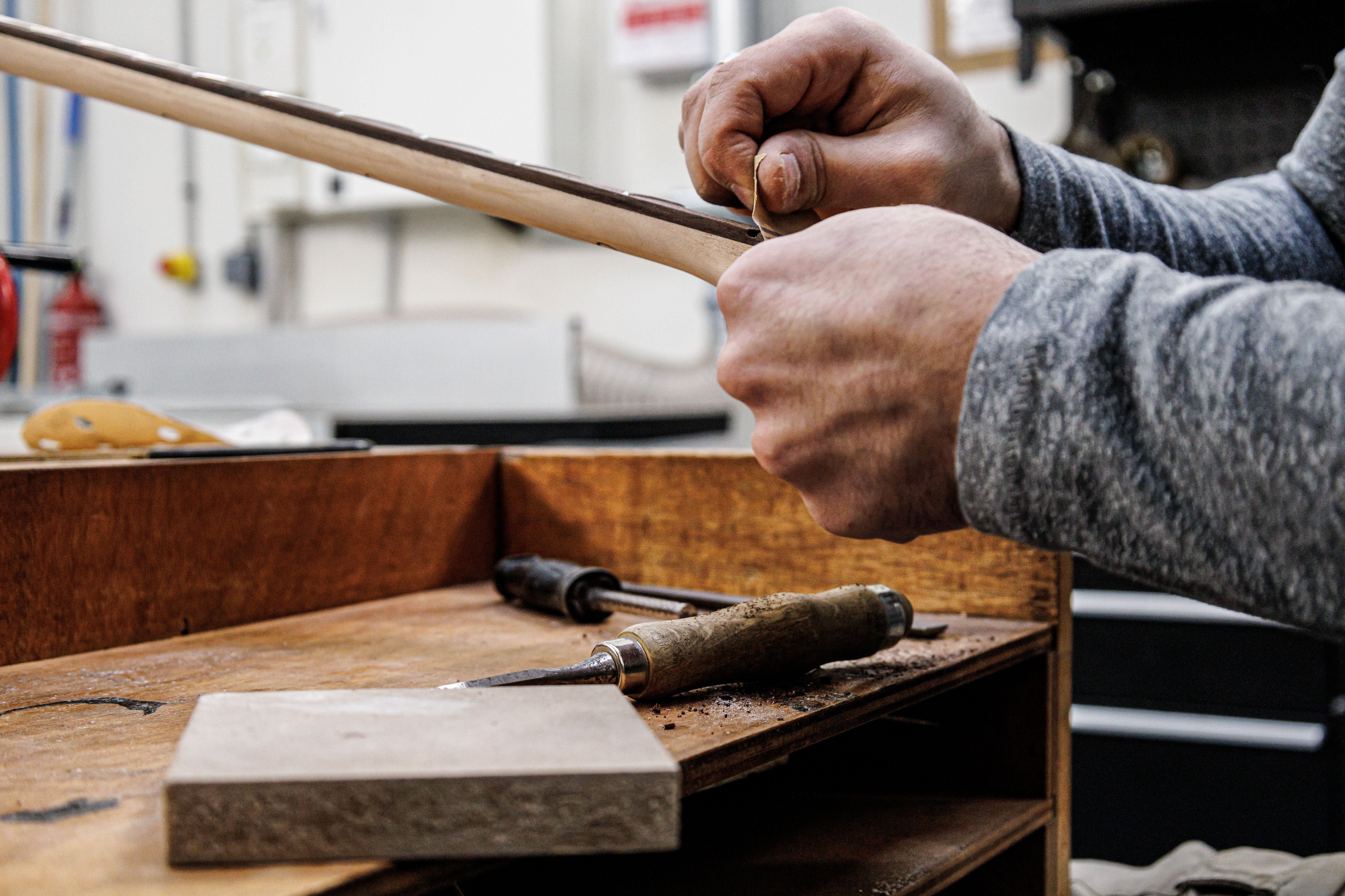 Hands of luthier Marin Belforti Nourry sanding a headstock, chisels and scrapers