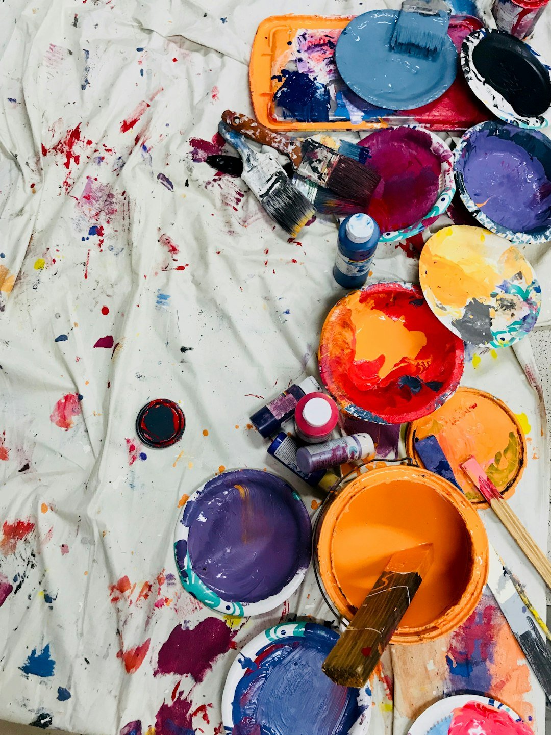 Color paints, brushes and paint containers on a white protective layer