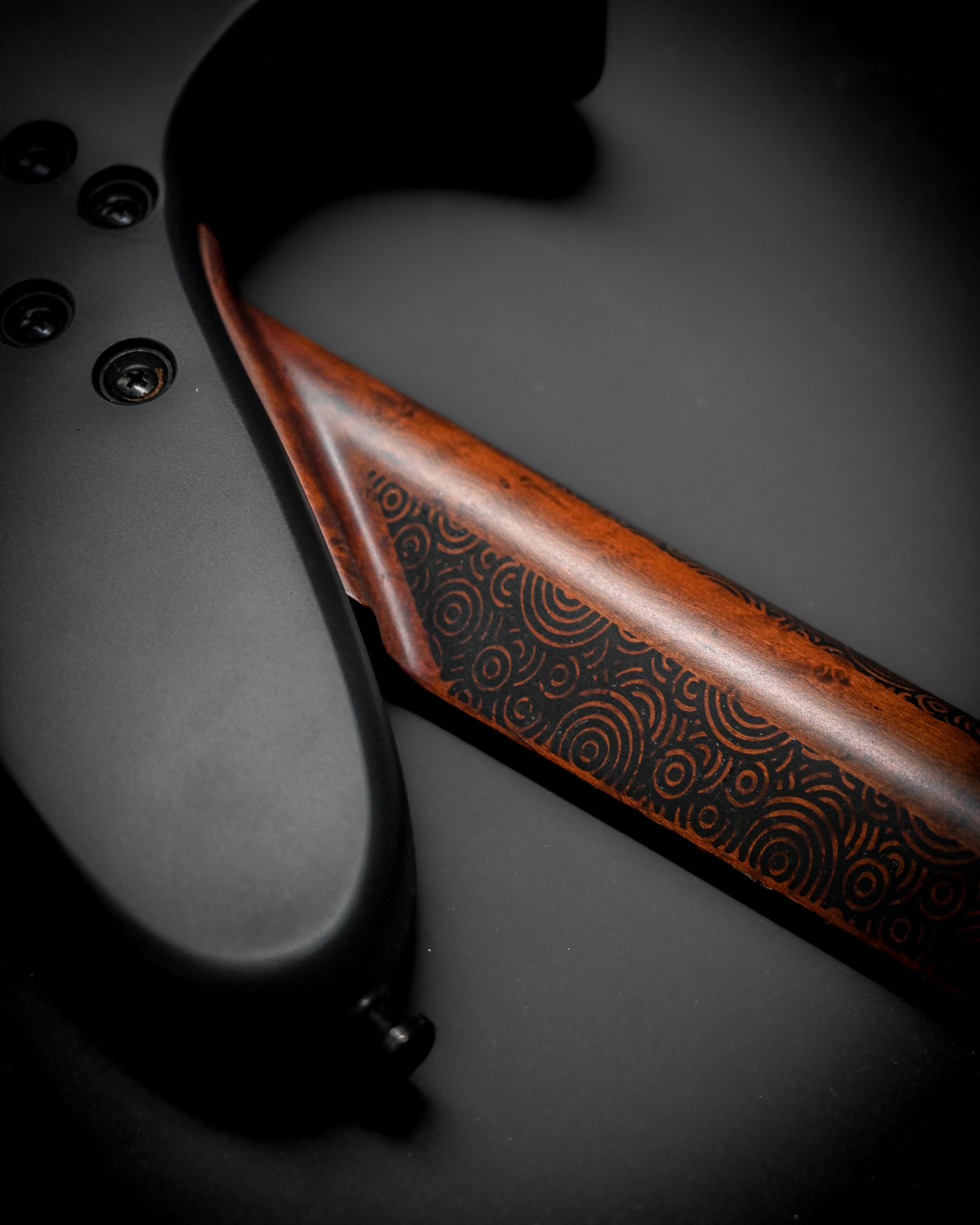 Close-up of a guitar neck with intricate wood pattern on a black background.