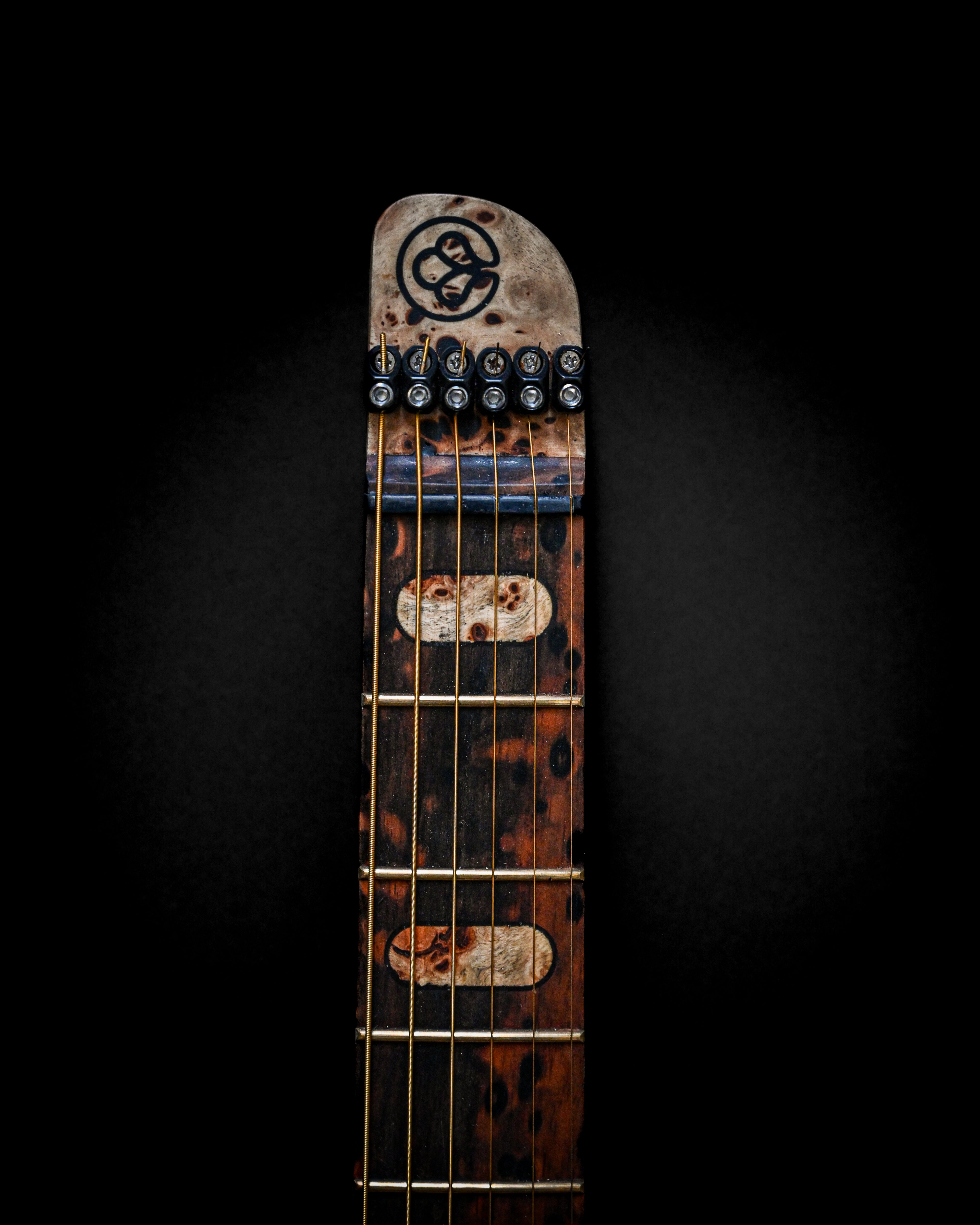 Rustic guitar neck with tribal design on headstock against black background