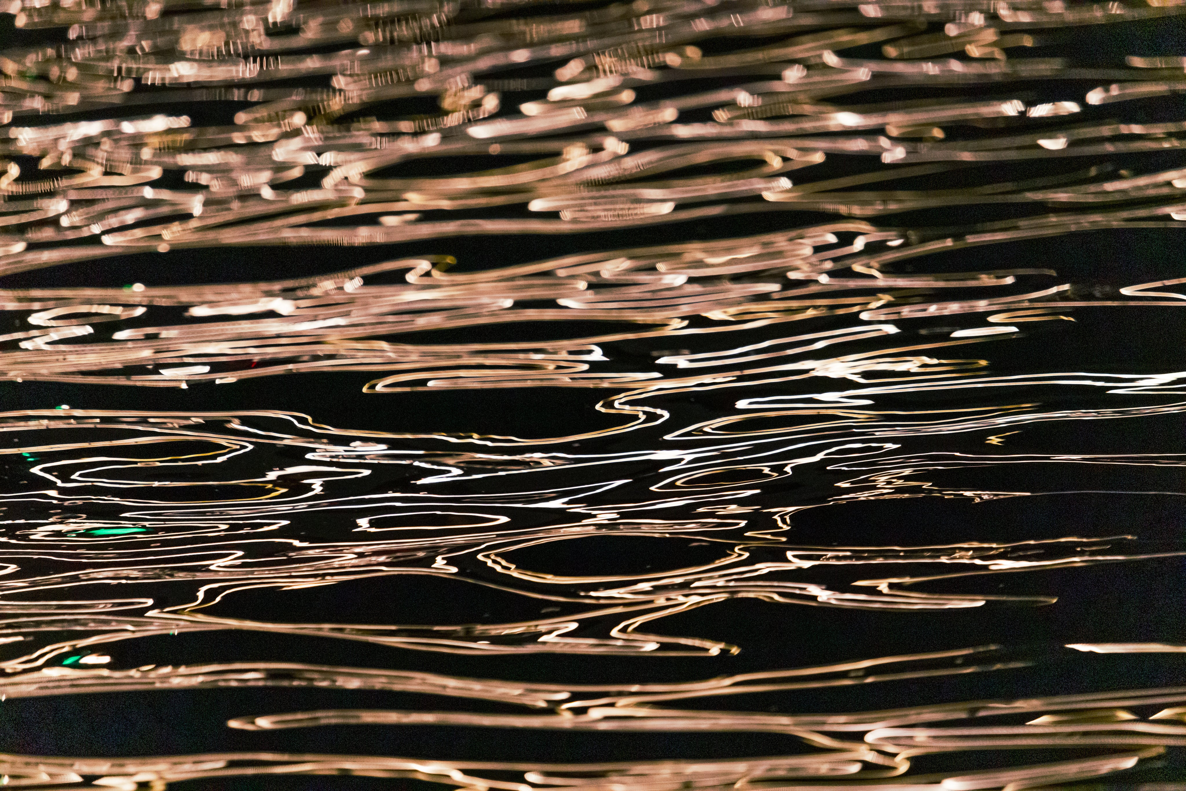 Rippling water with reflective light patterns creating an abstract design effect on a dark surface.