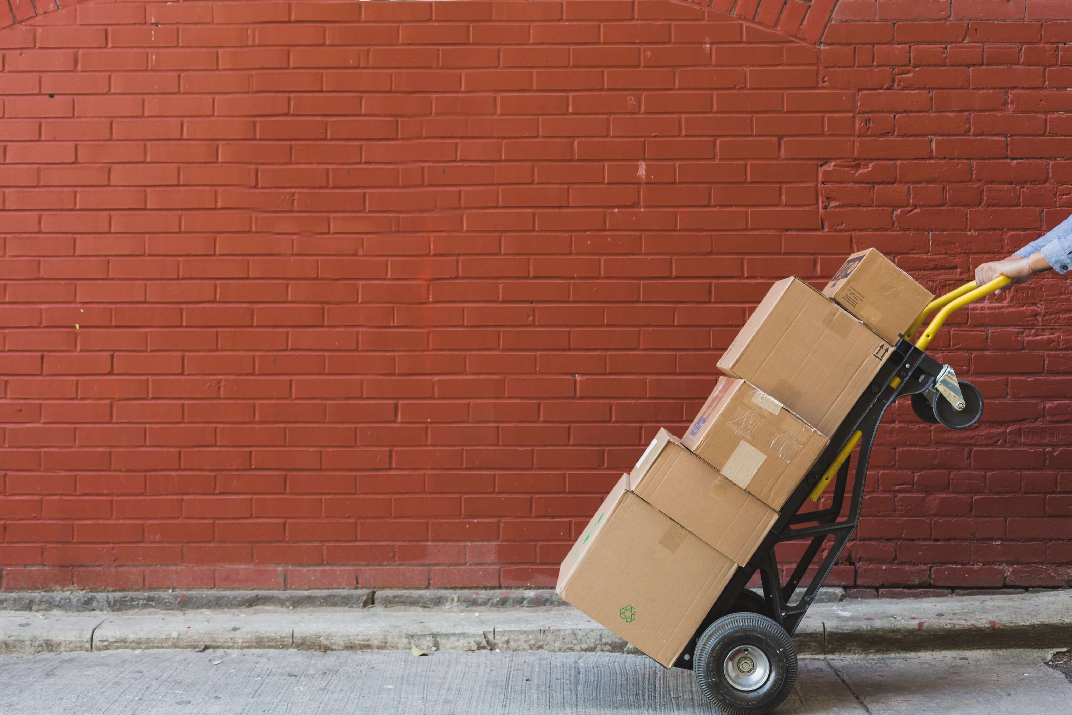 Person pushing a hand truck loaded with boxes against a red brick wall