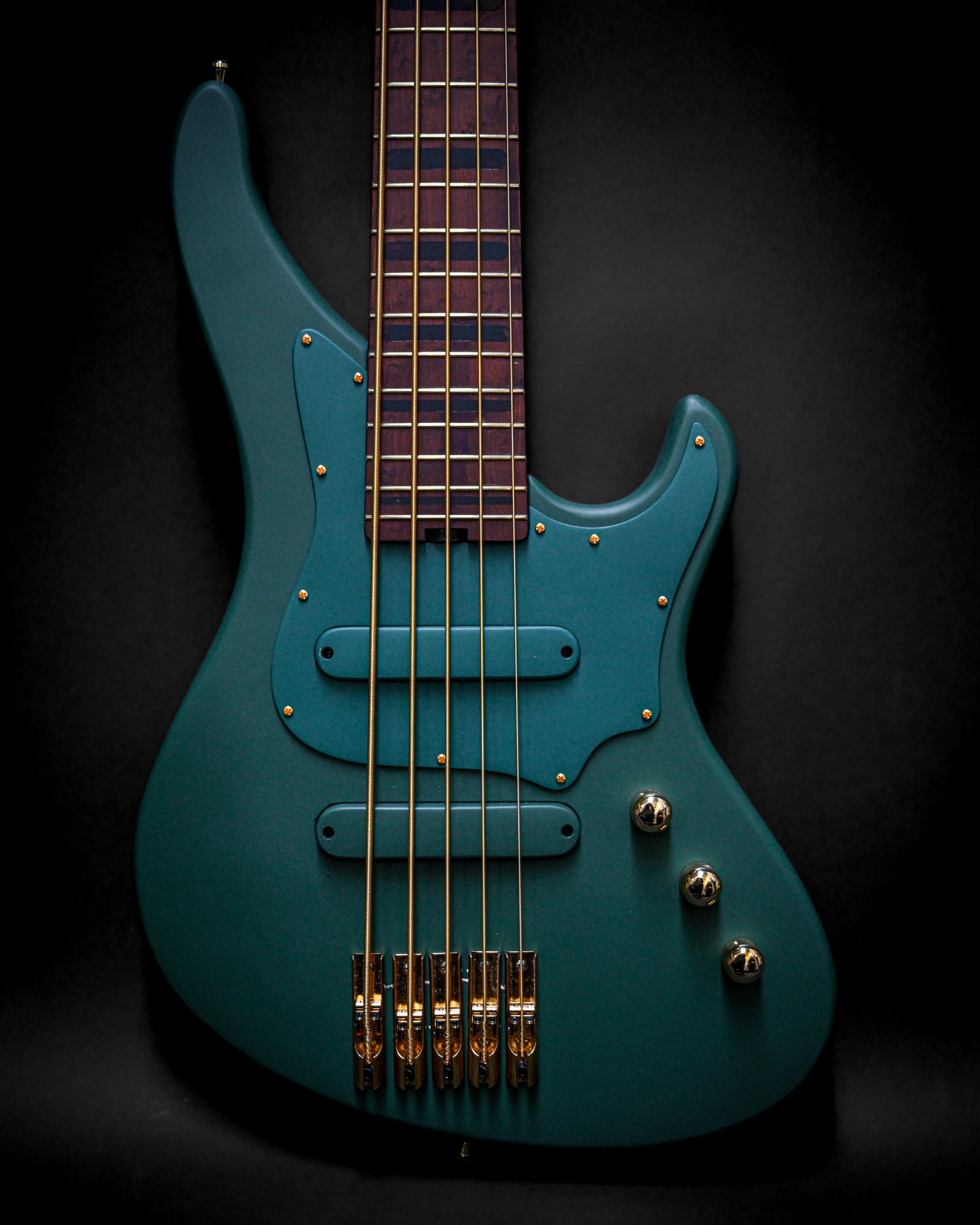 Guitarra eléctrica Belforti en acabado verde azulado con herrajes dorados sobre un fondo negro, que muestra un diseño moderno y detalles de artesanía.