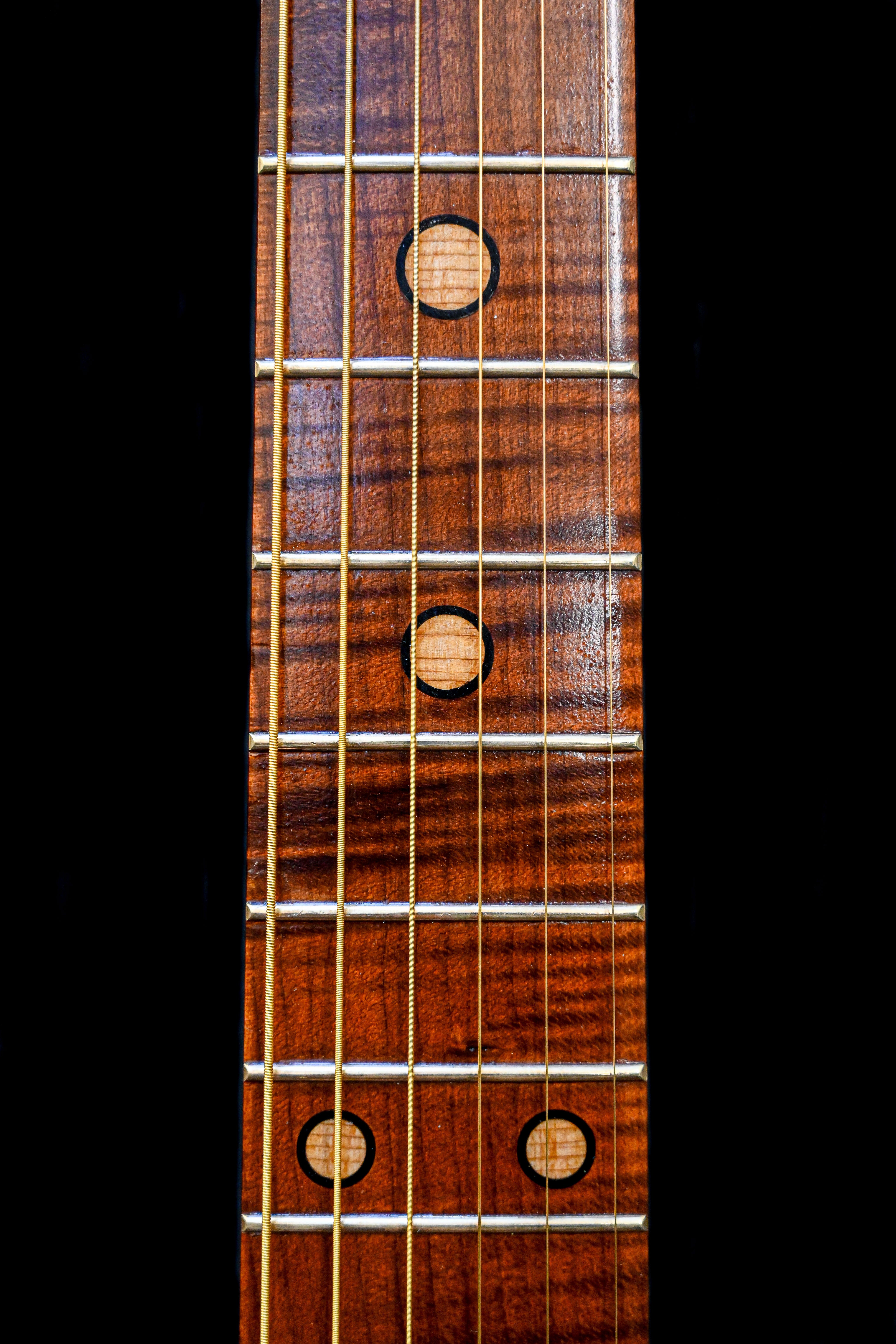 Primer plano del diapasón de la guitarra M7 Heritage Red Cedar de Belforti Instruments, que destaca el diseño único de las incrustaciones y las cuerdas pulidas.