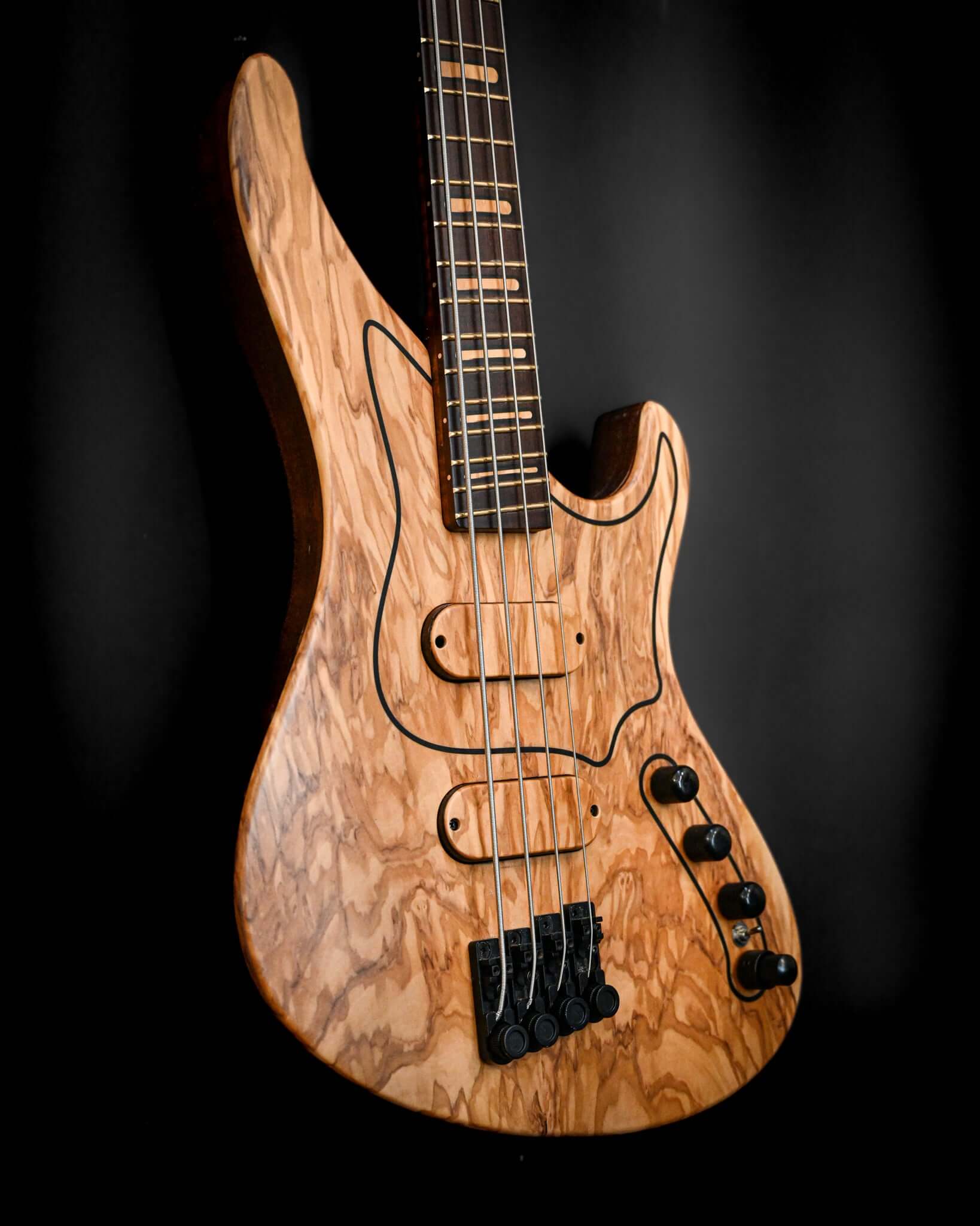 Bajo eléctrico M1 HL/SS - Olivo Italiano con una impresionante tapa de madera de olivo, que muestra un diseño sin clavijero y de escala corta para facilitar la ejecución.