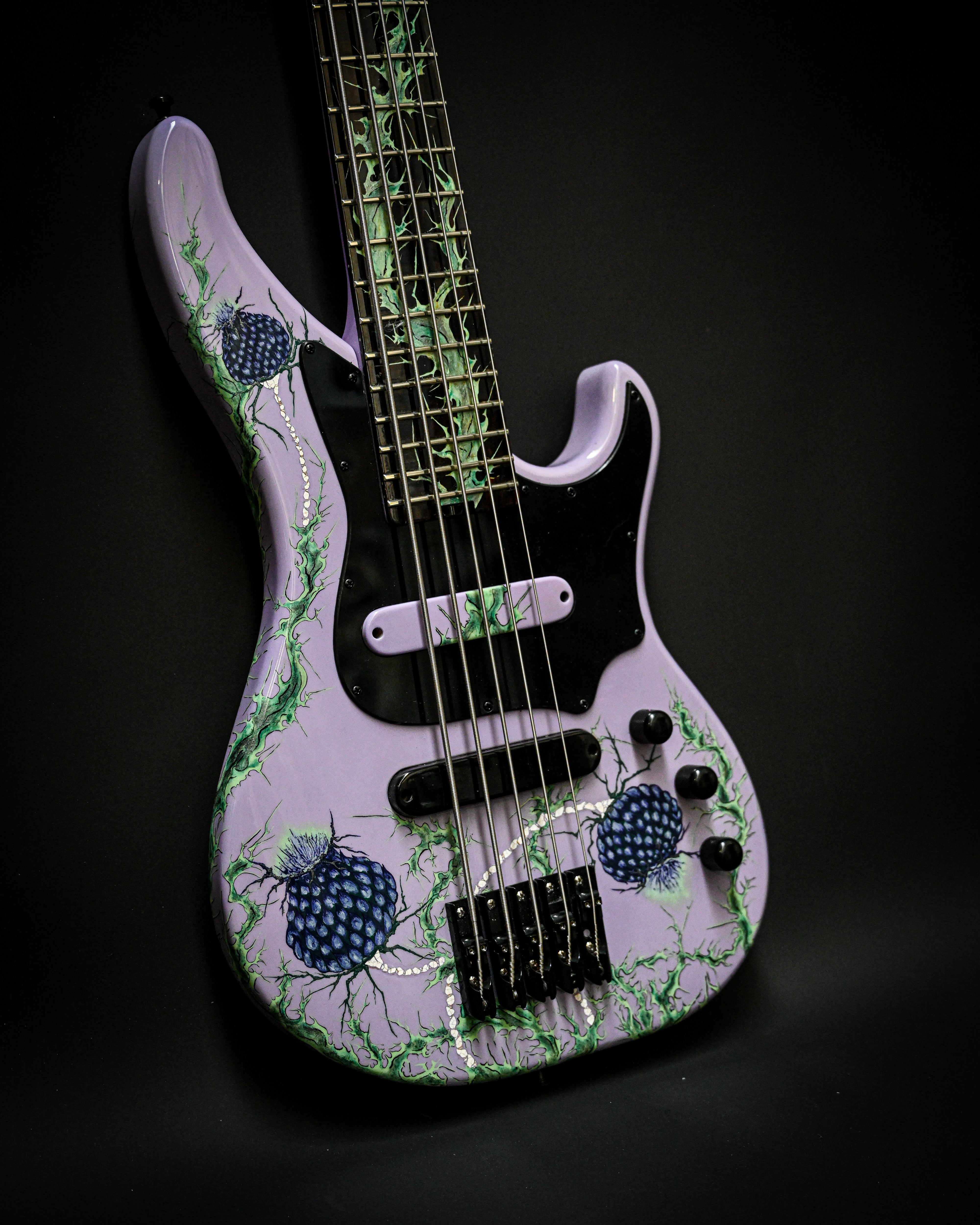 Bajo eléctrico morado con diseño floral, con intrincados dibujos verdes y azules sobre fondo oscuro.