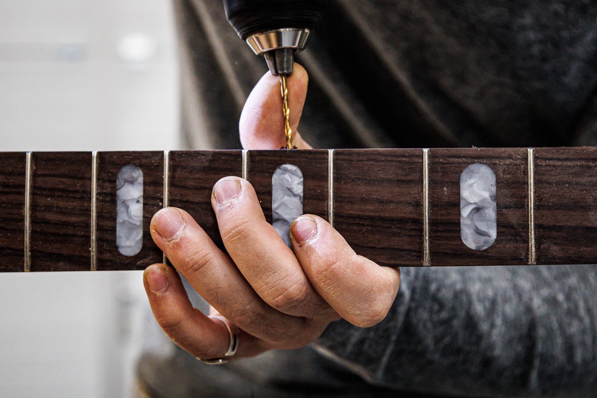 Gros plan sur les mains du luthier Marin Nourry-Belforti perçant des points latéraux sur la touche d'une basse E1.