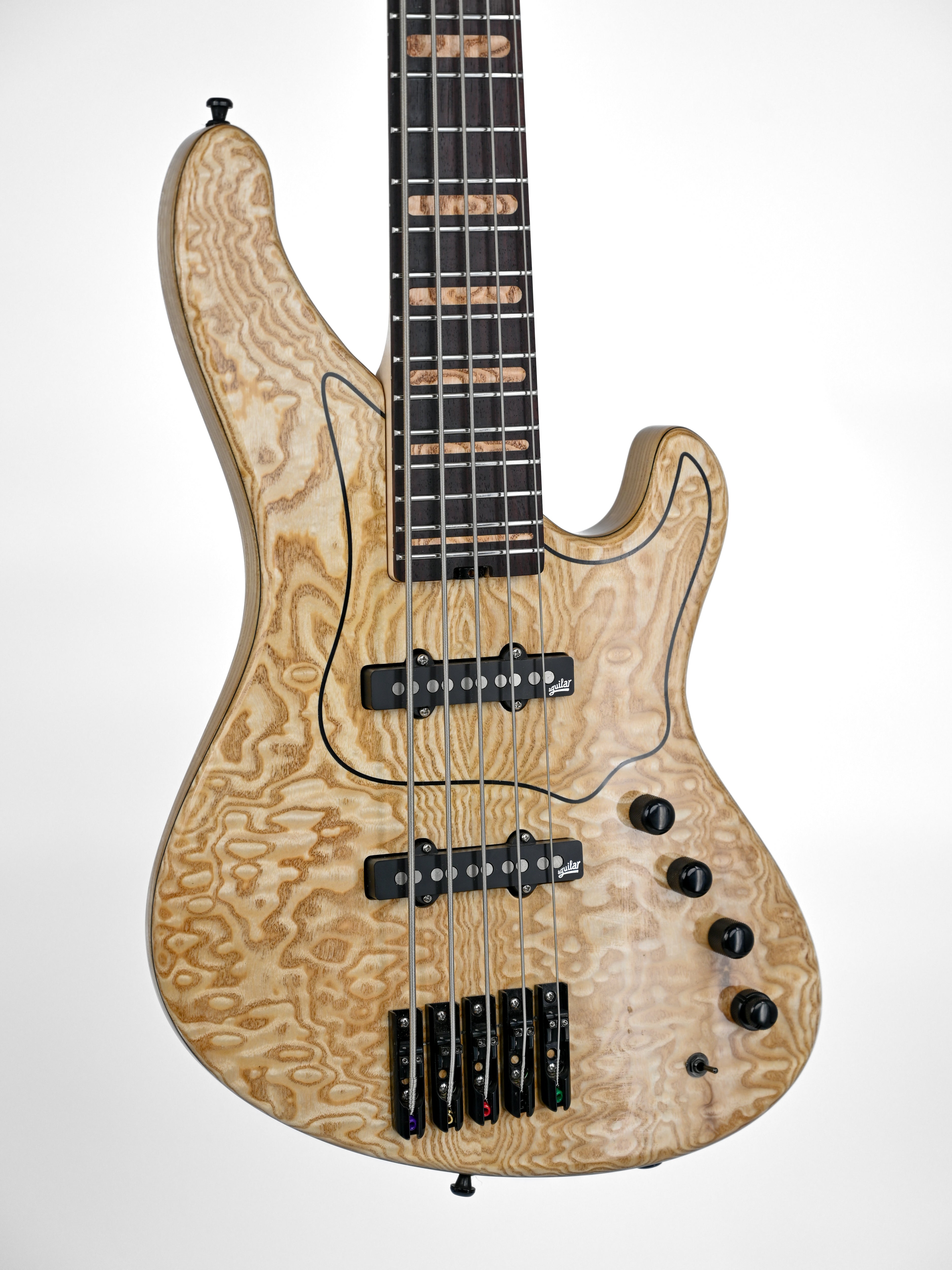 Guitare basse électrique à cinq cordes avec une finition en bois naturel et des micros noirs sur fond blanc.