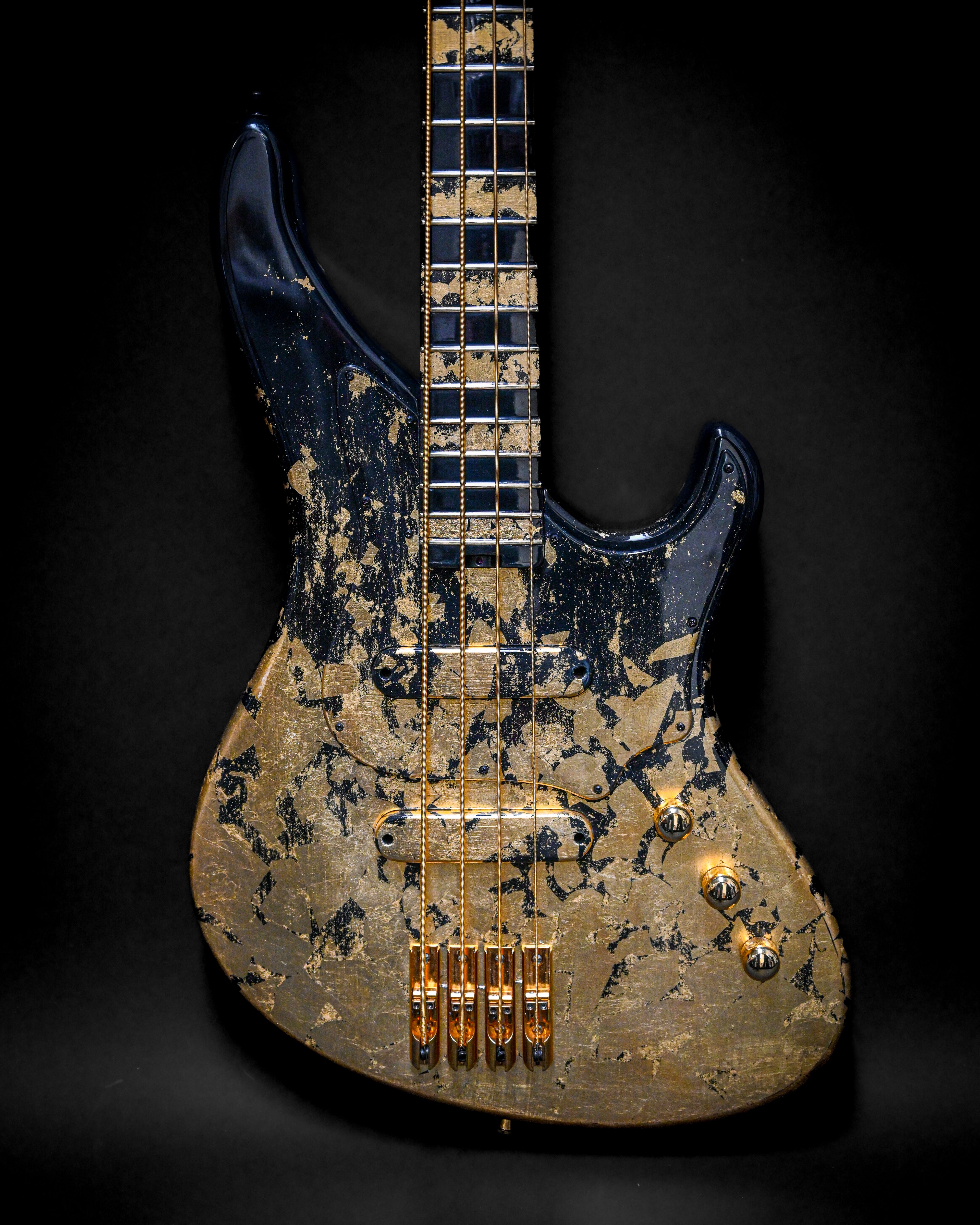 Gros plan d'une guitare basse électrique personnalisée avec un design noir et or sur un fond sombre.