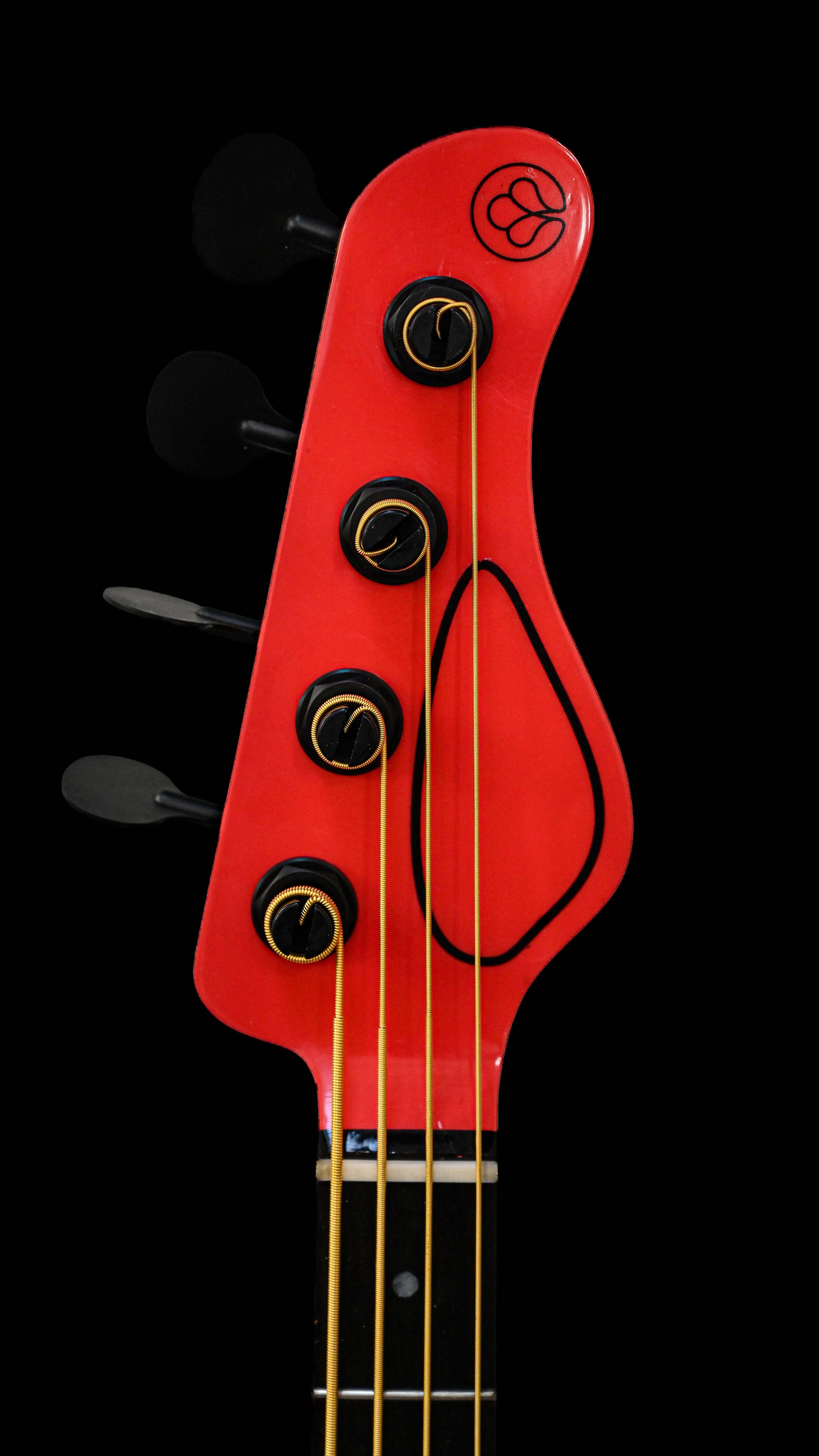 Belforti InstrumentsのE1 Normandy Apple Redベースギターのヘッドストックの詳細な画像。ユニークなデザインと鮮やかな配色が目を引きます。