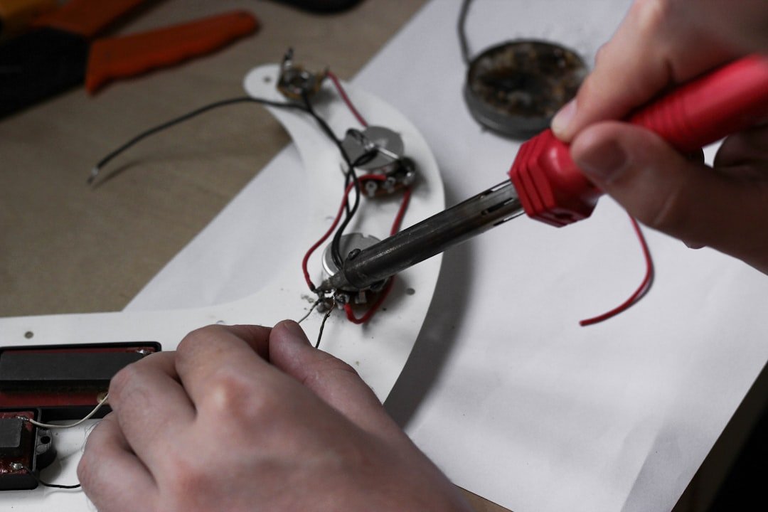Um plano aproximado de uma pessoa a soldar componentes de guitarra num guarda-unhas