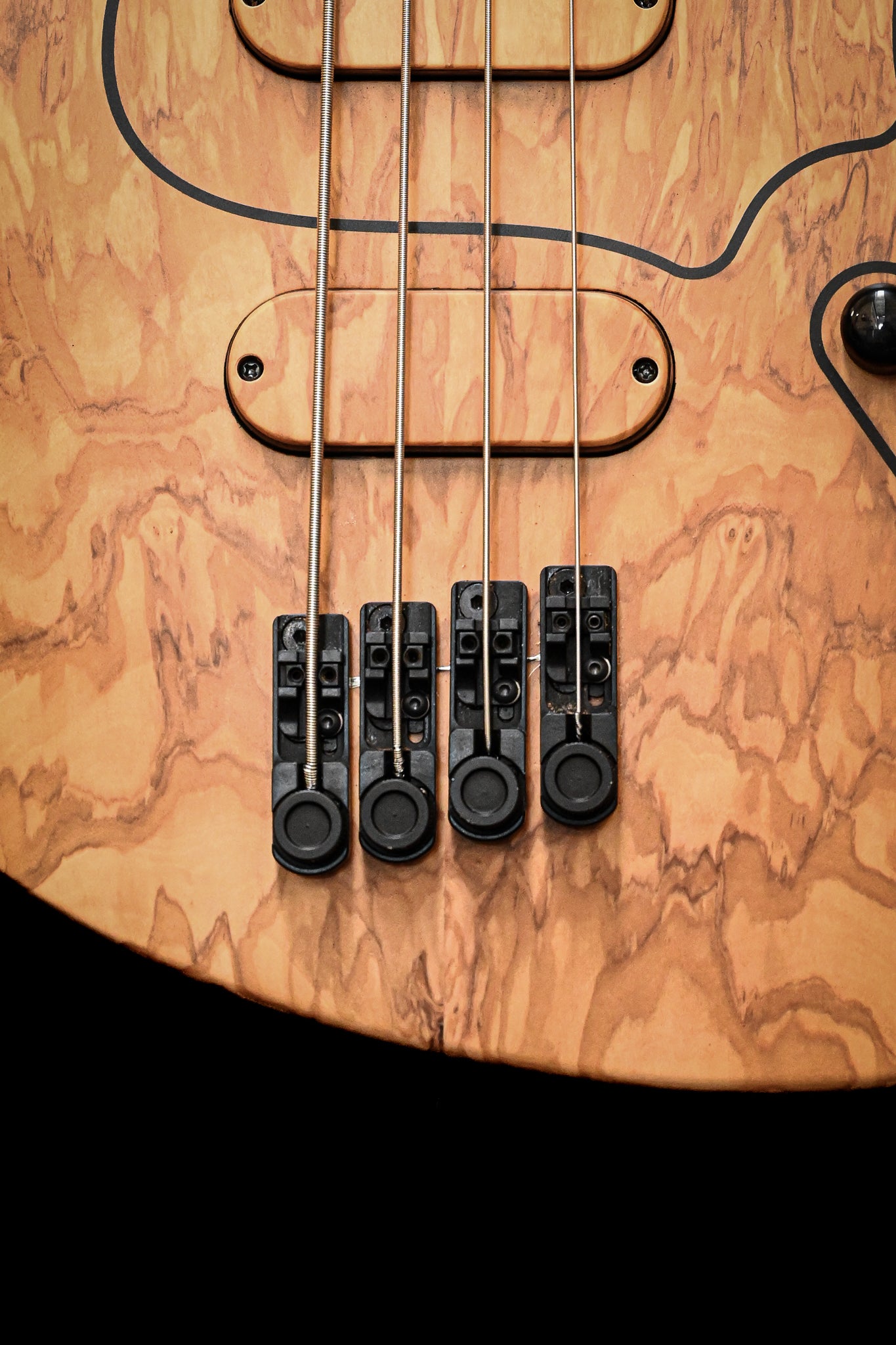 Close-up of a four-string electric bass guitar with a natural wood finish, highlighting the strings and bridge.