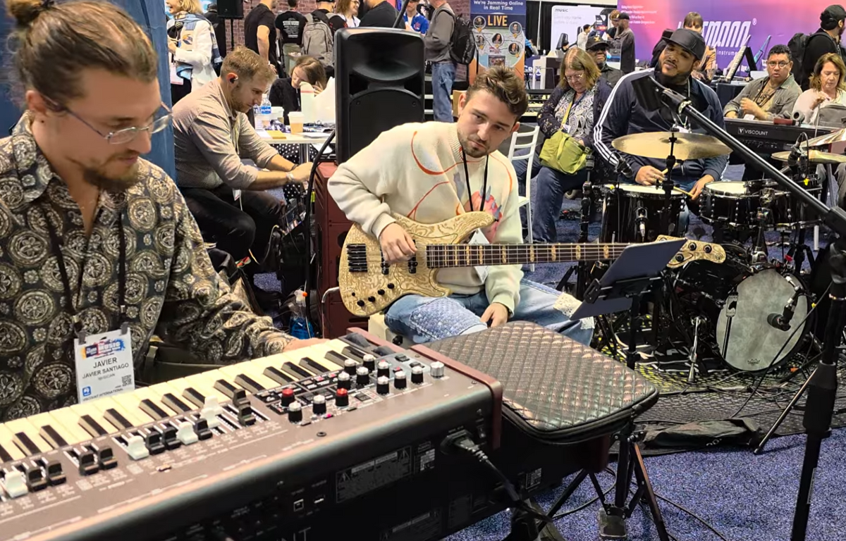 Musicians playing keyboard, bass, and drums at a lively music event with an audience in the background.