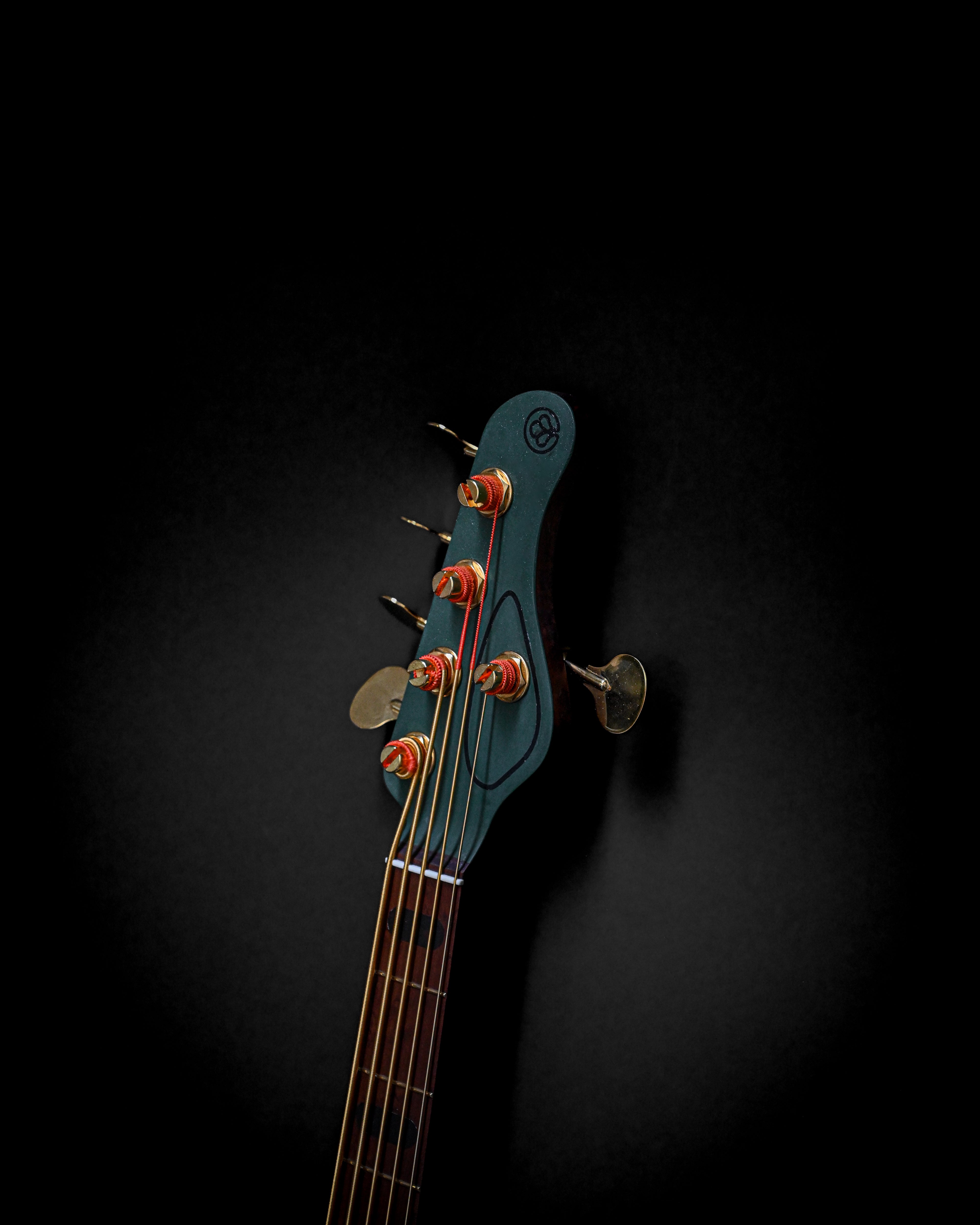 Close-up of a bass guitar headstock with strings and tuning pegs on a dark background.