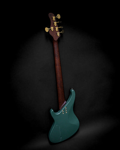 Back view of a teal electric bass guitar with a dark wood neck and gold tuning pegs on a black background.