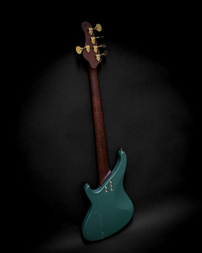 Back view of a teal electric bass guitar with a dark wood neck and gold tuning pegs on a black background.
