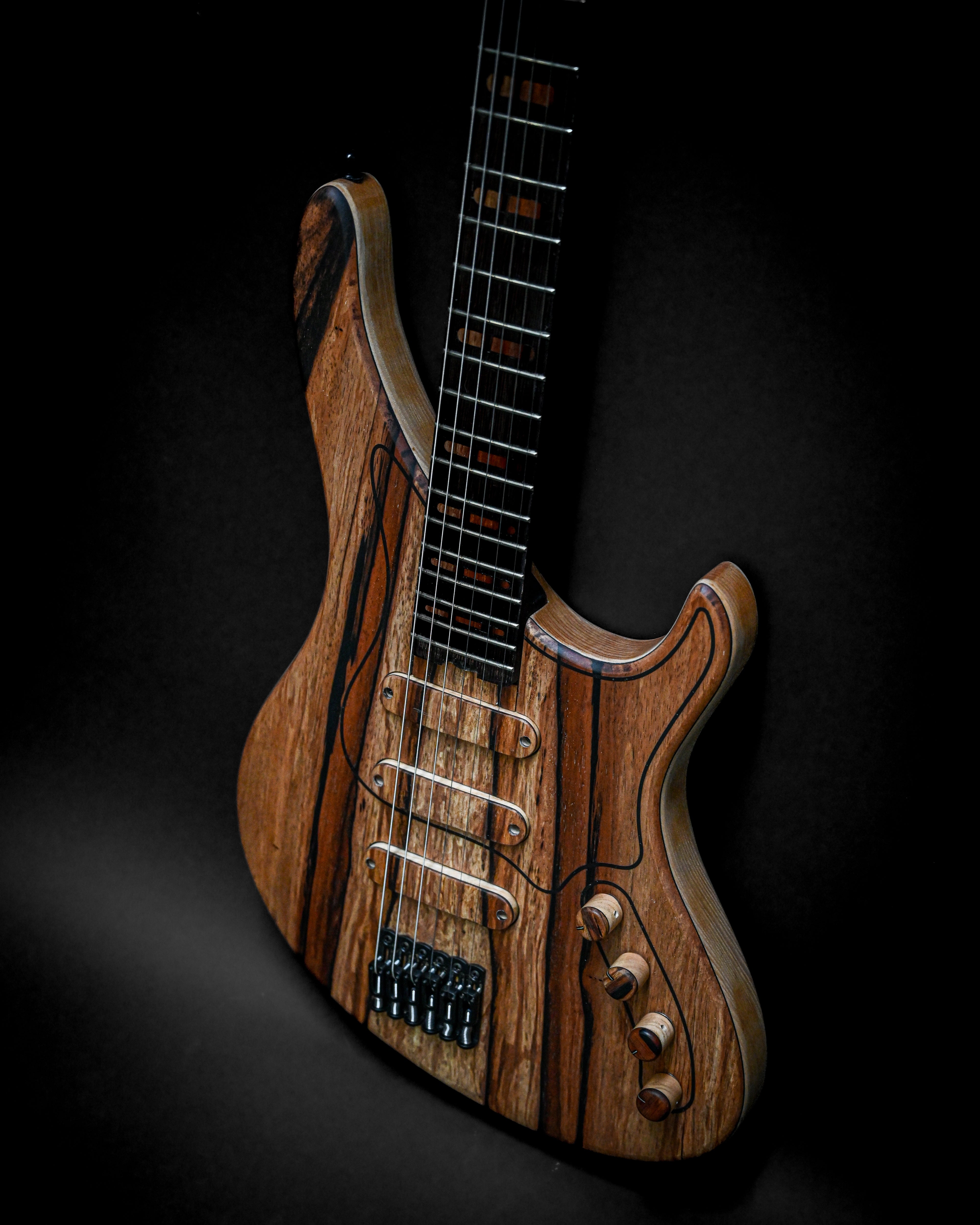 Electric guitar with a natural wood finish and three pickups, against a dark background.