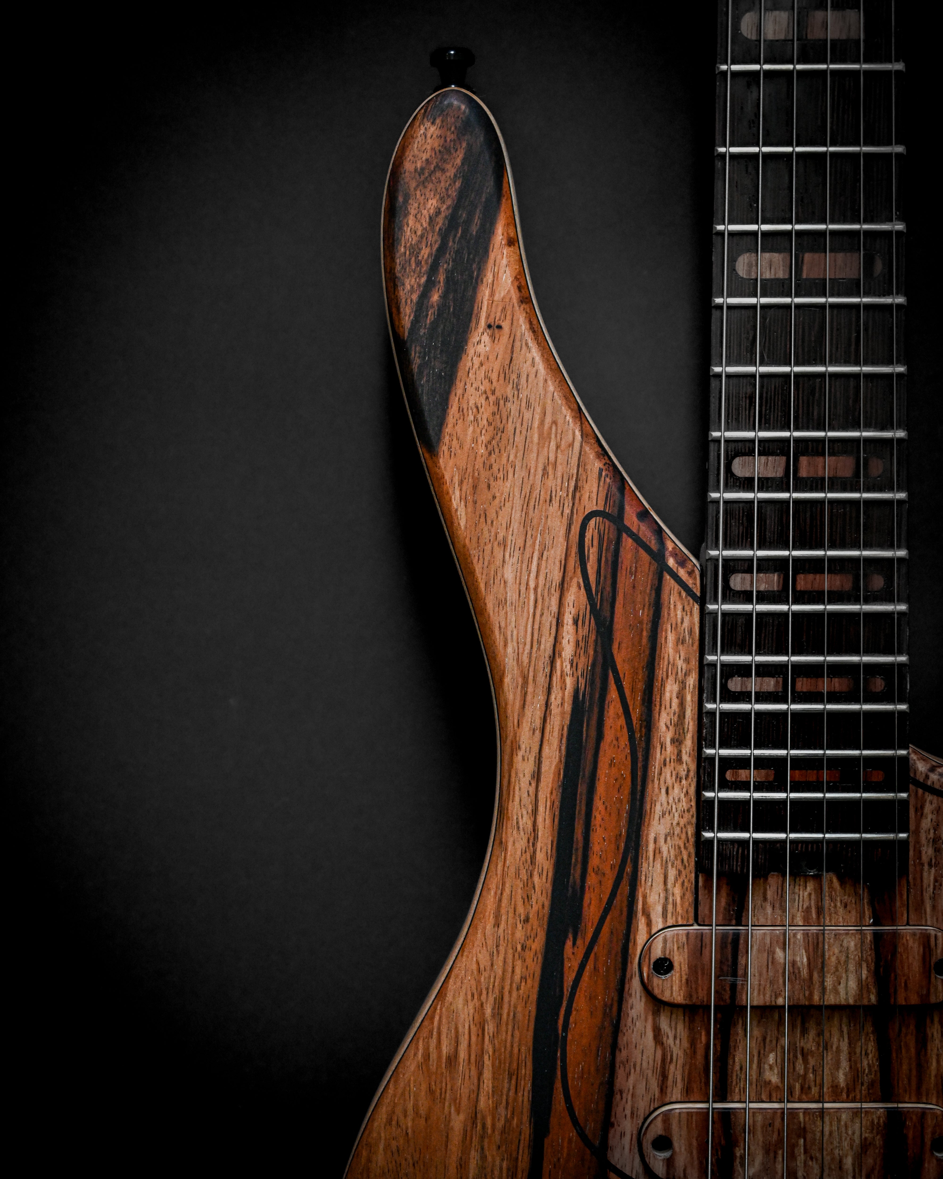 Close-up of a wooden electric guitar neck and body against a dark background, highlighting intricate wood grain and craftsmanship.