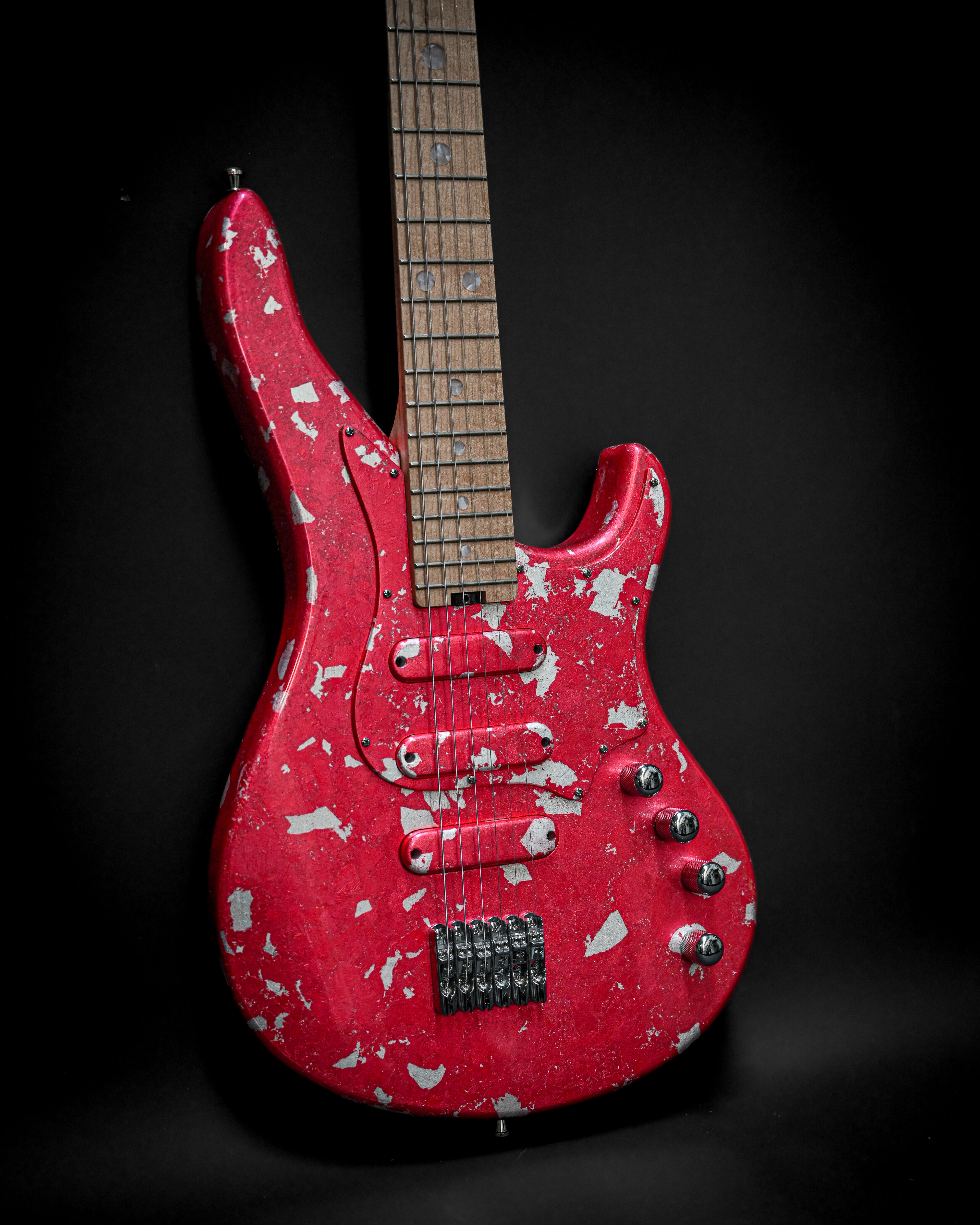 Red electric guitar with a distressed finish and wooden fretboard against a dark background.