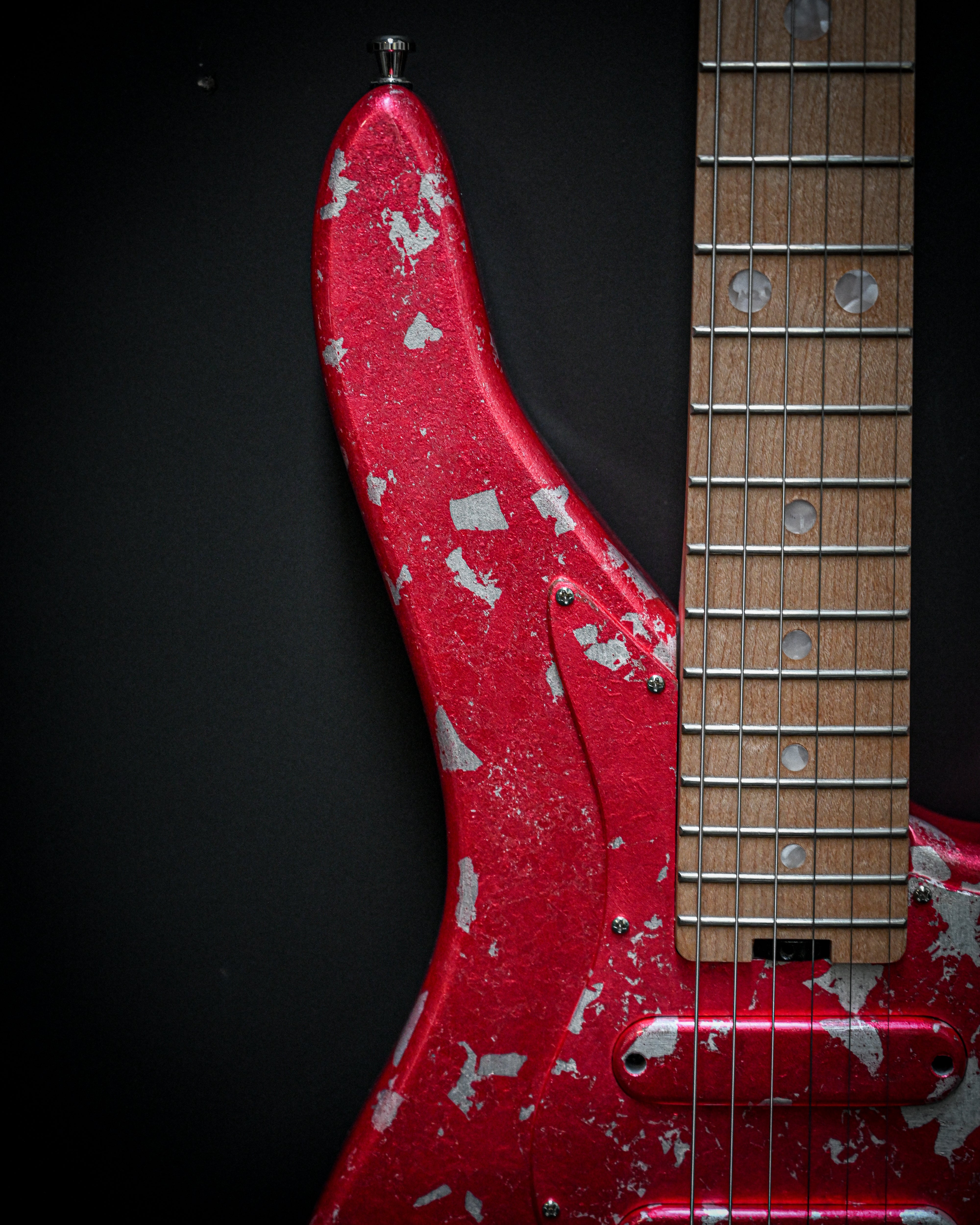 Close-up of a red electric guitar with a worn finish and maple fretboard on a black background.