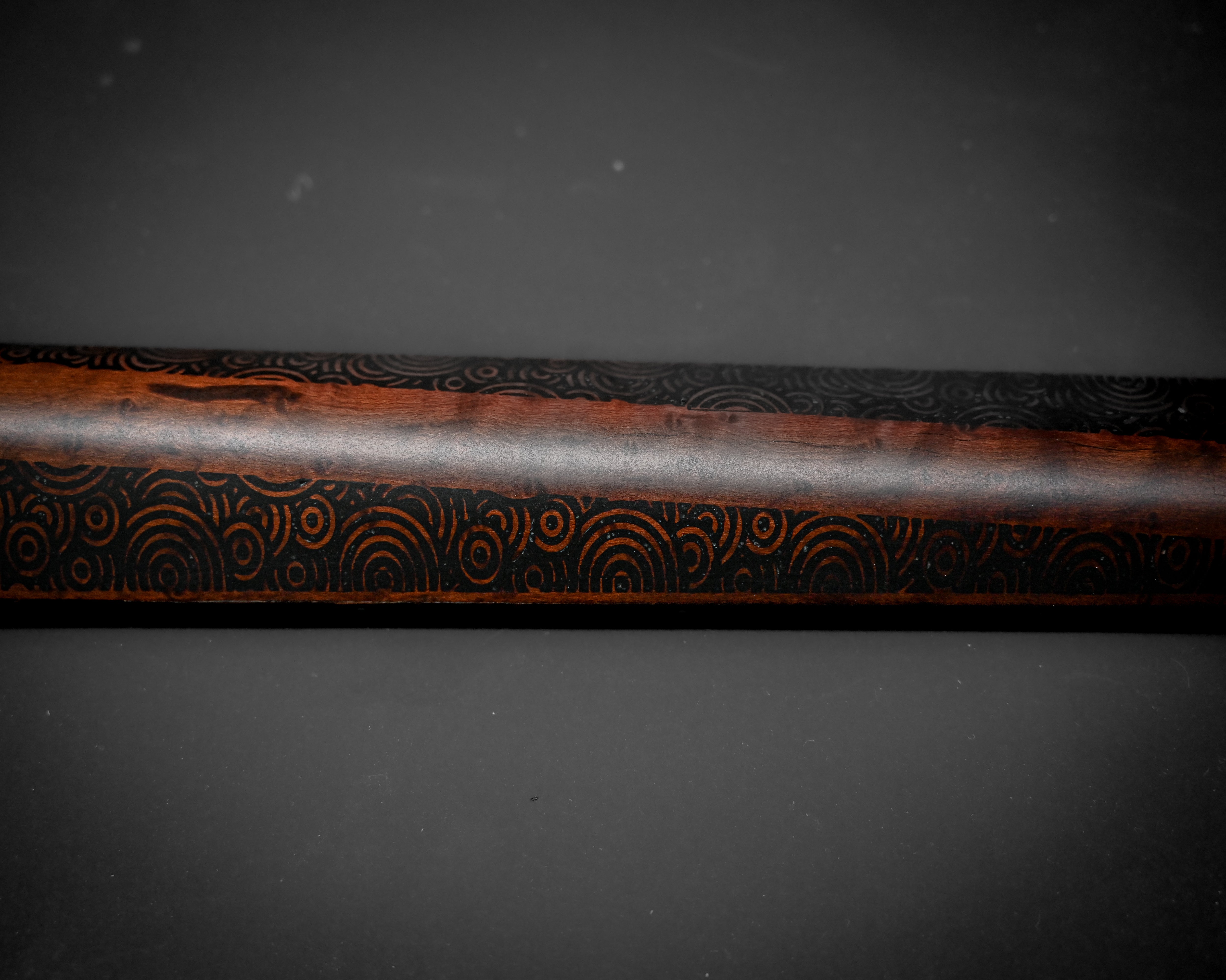 Close-up of a wooden bat with intricate black circular patterns on a dark background.