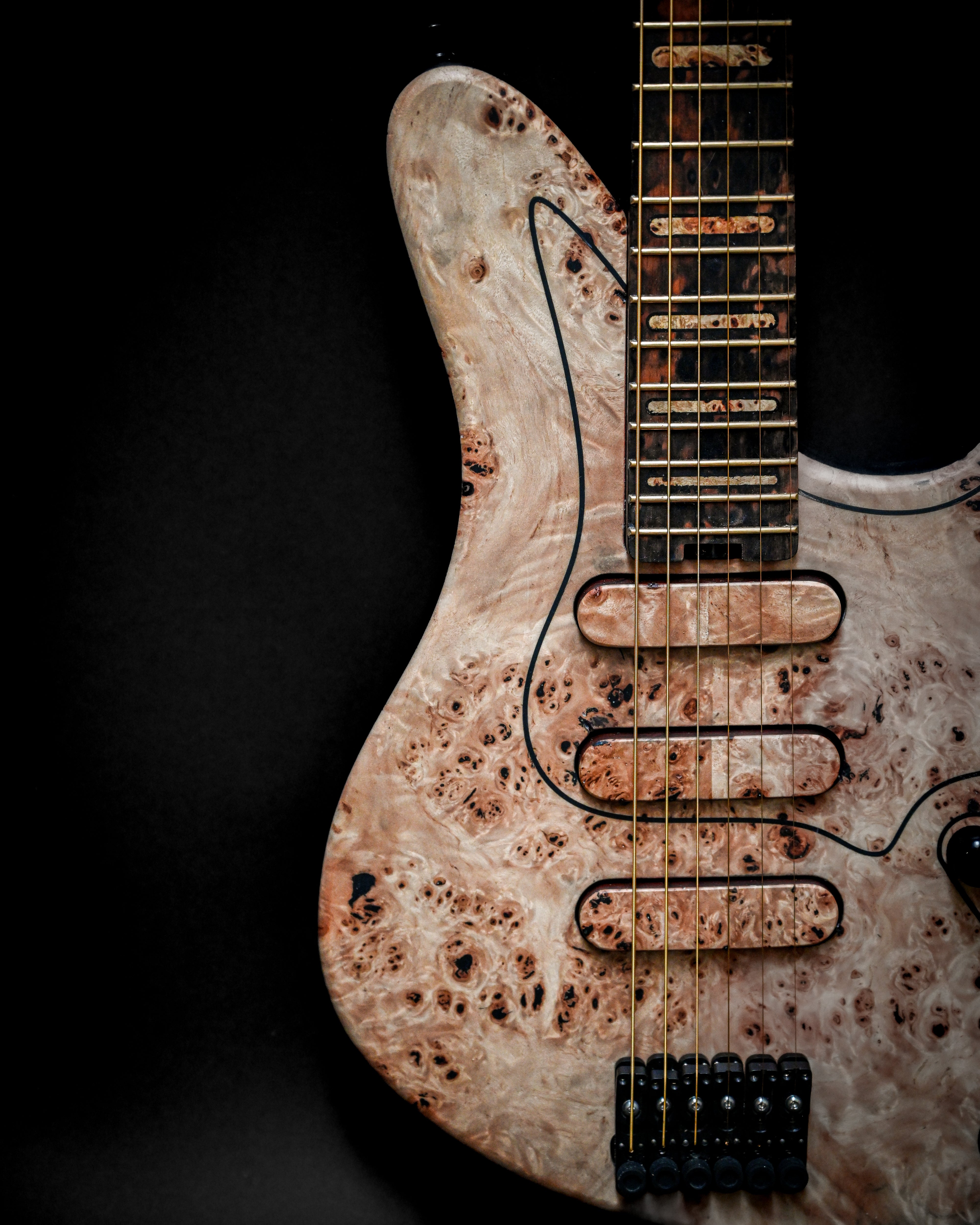 Close-up of an electric guitar with a unique wood grain finish and gold frets against a dark background.