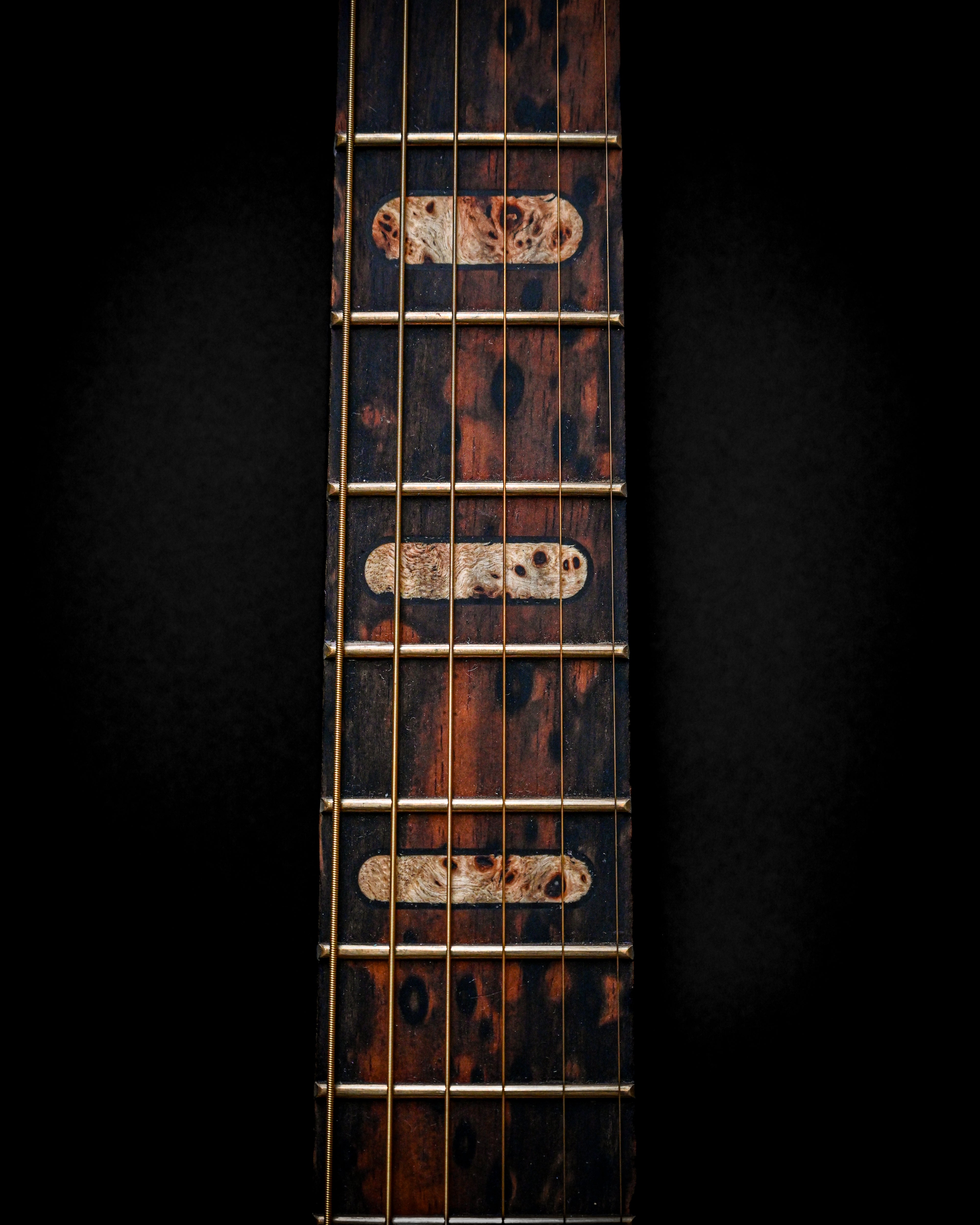 Close-up of a vintage guitar neck with unique fretboard design on a dark background.
