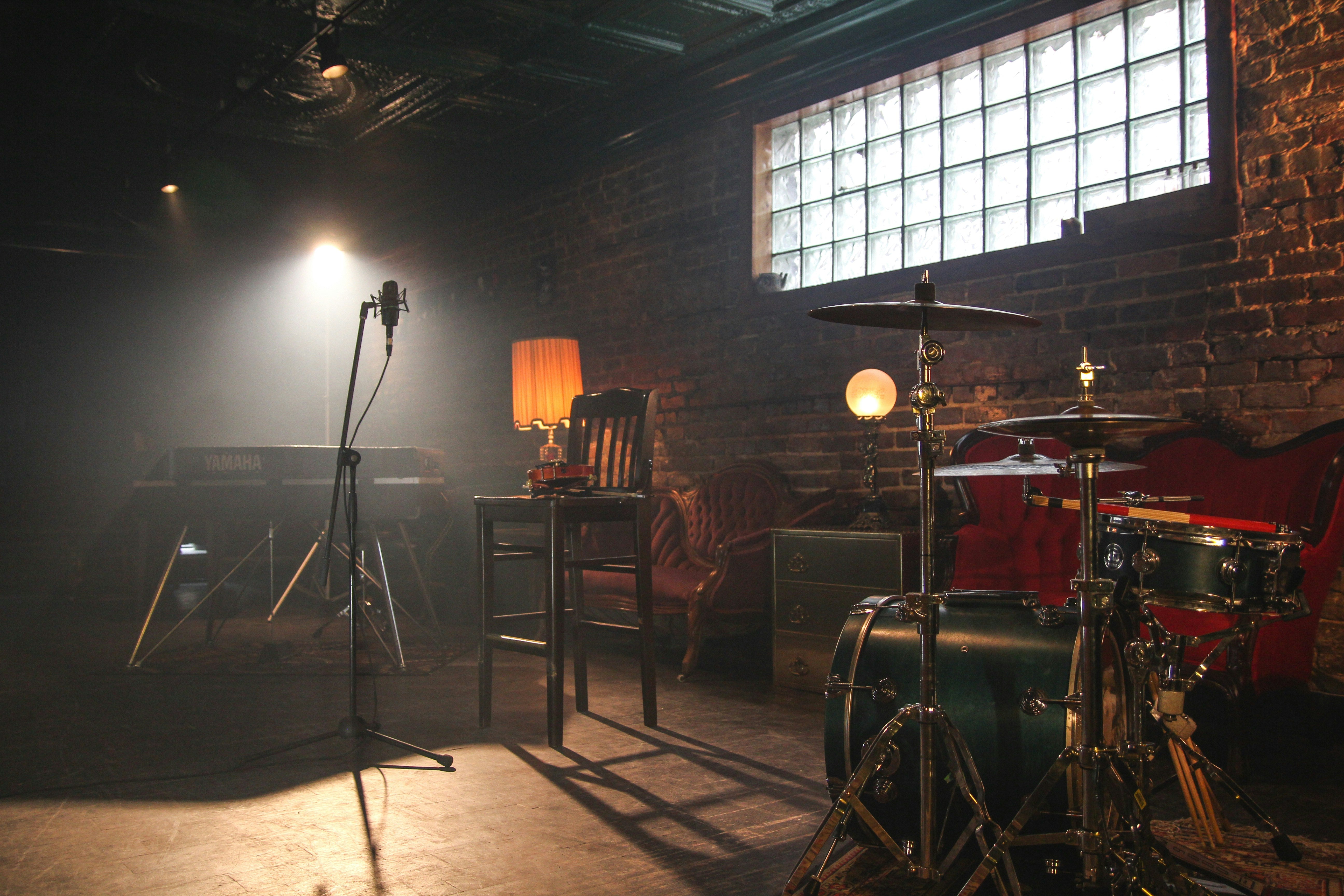 A quiet stage in a room with brick walls, sofas, drumkit and mics