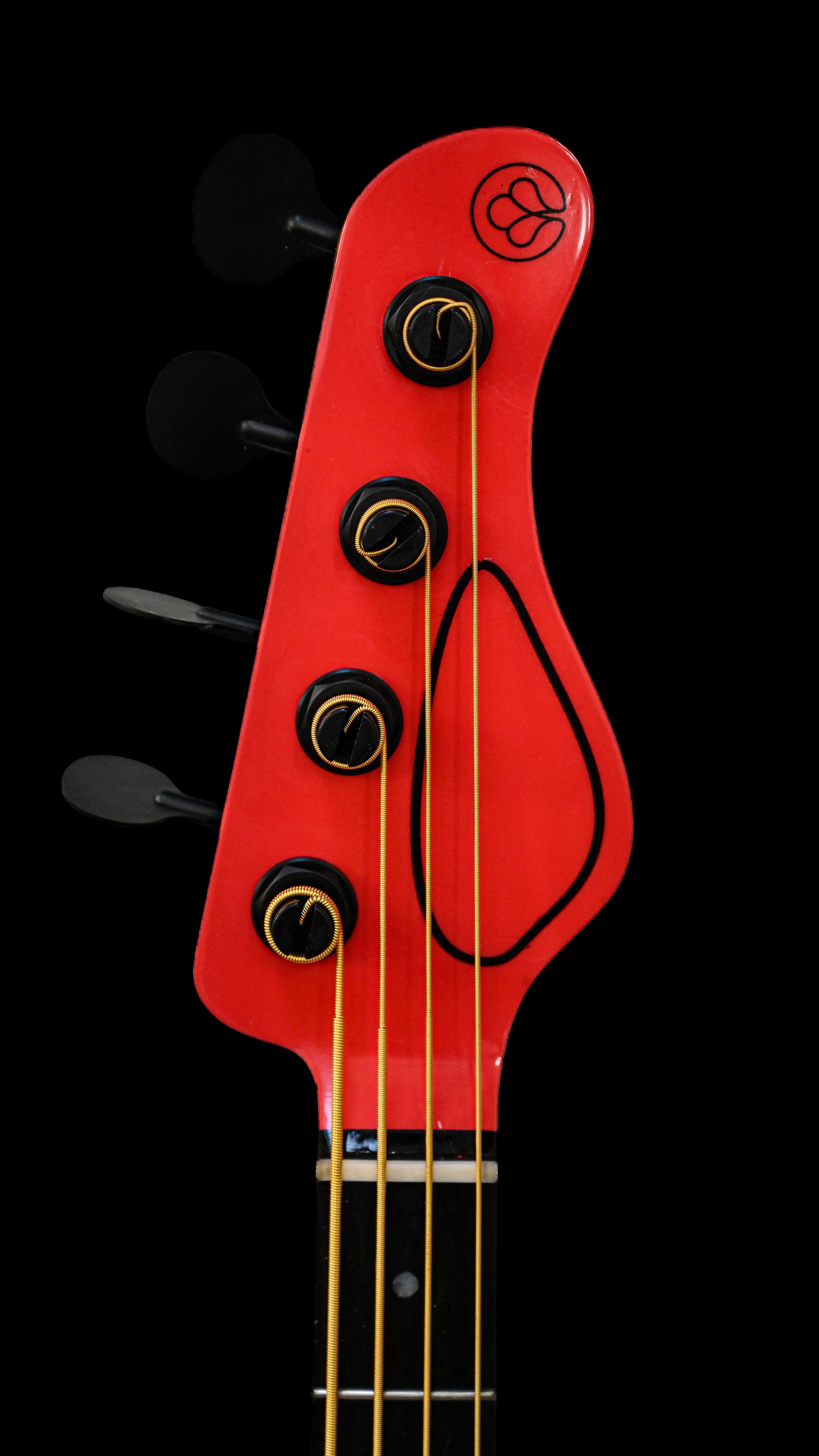 Detailansicht der Kopfplatte der E1 Normandy Apple Red Bassgitarre von Belforti Instruments, die das einzigartige Design und die leuchtende Farbgebung zeigt.