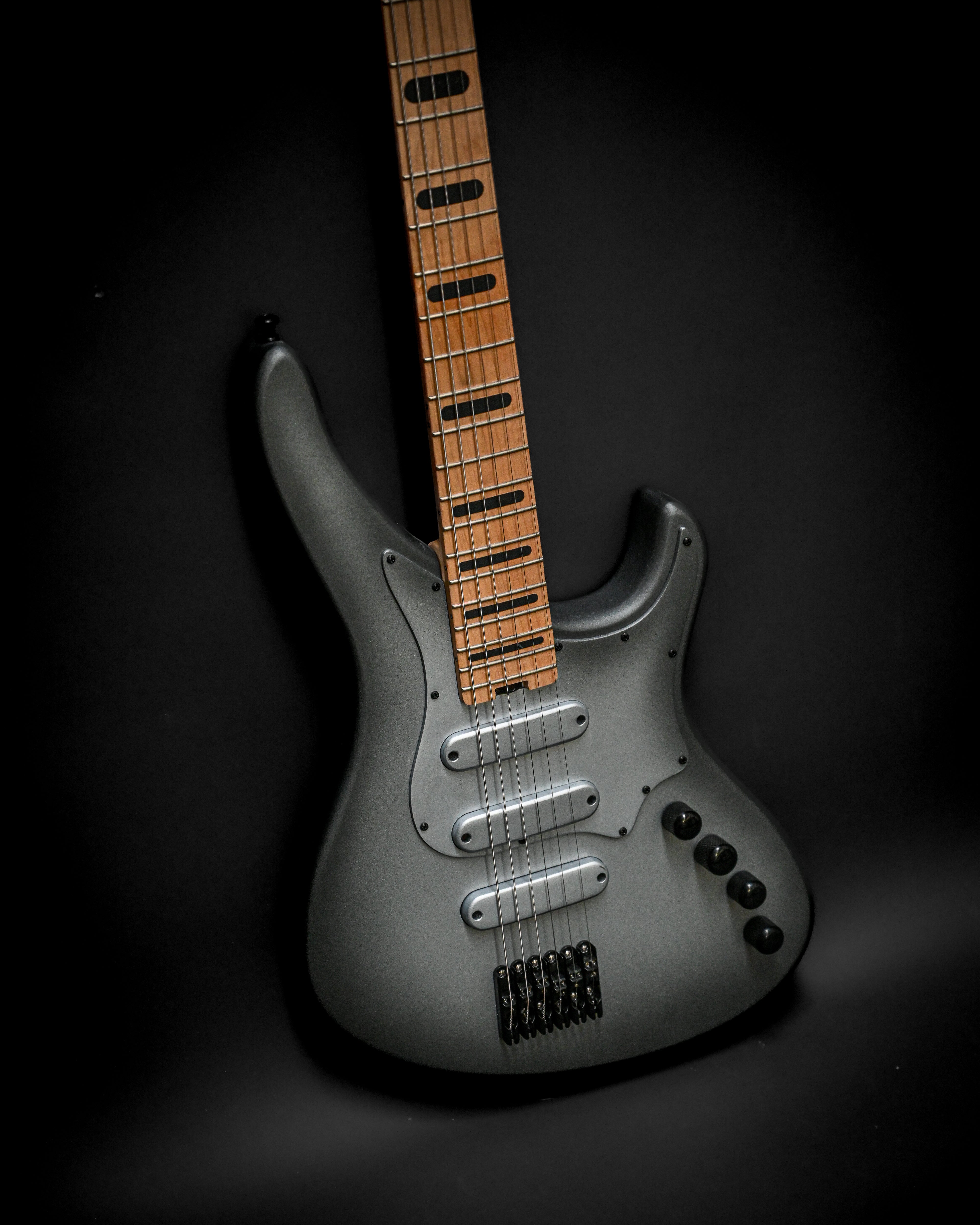 Guitare électrique noire élégante avec touche en bois et plusieurs micros sur fond sombre.