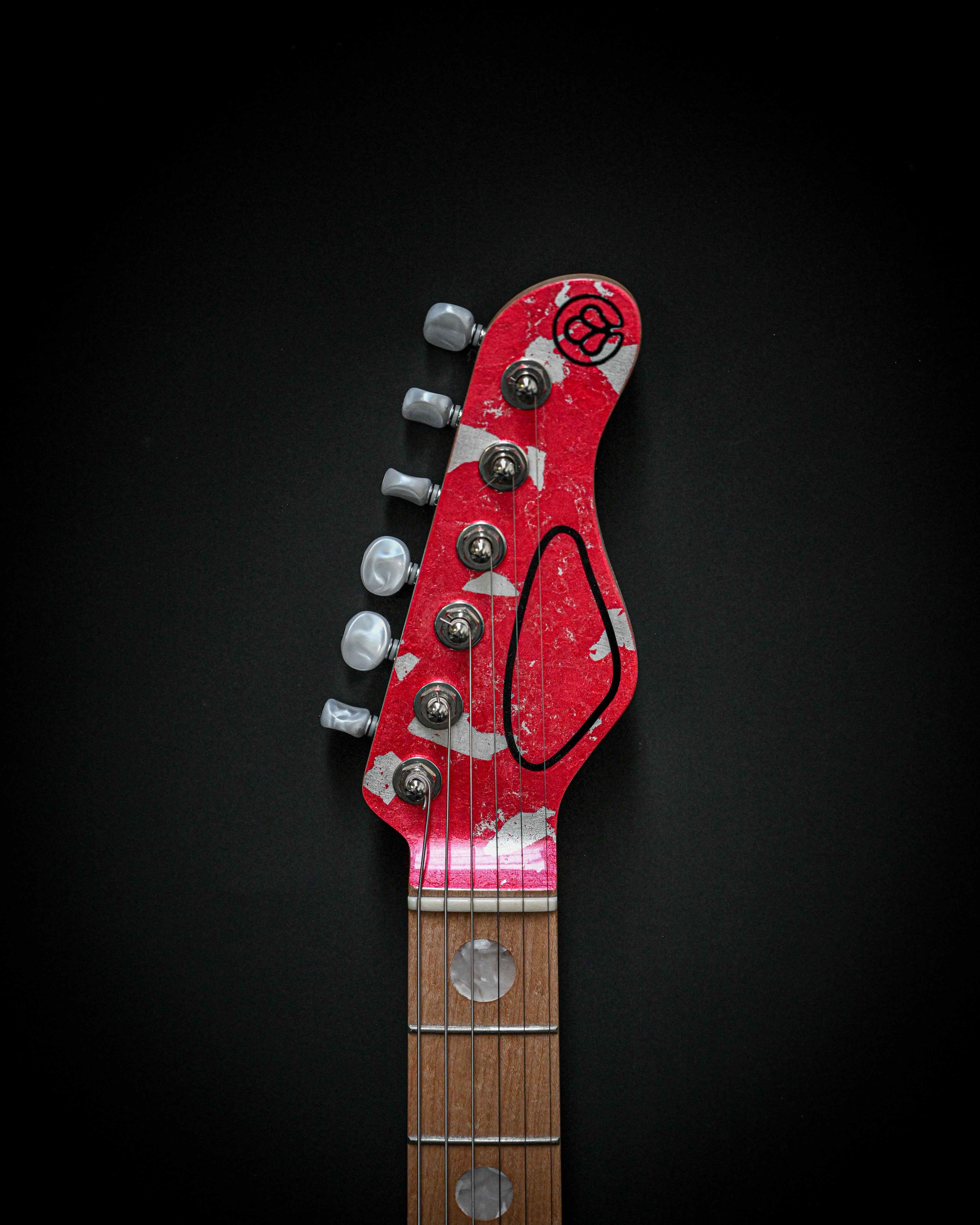 Tête de guitare électrique rouge avec chevilles d'accordage sur fond noir